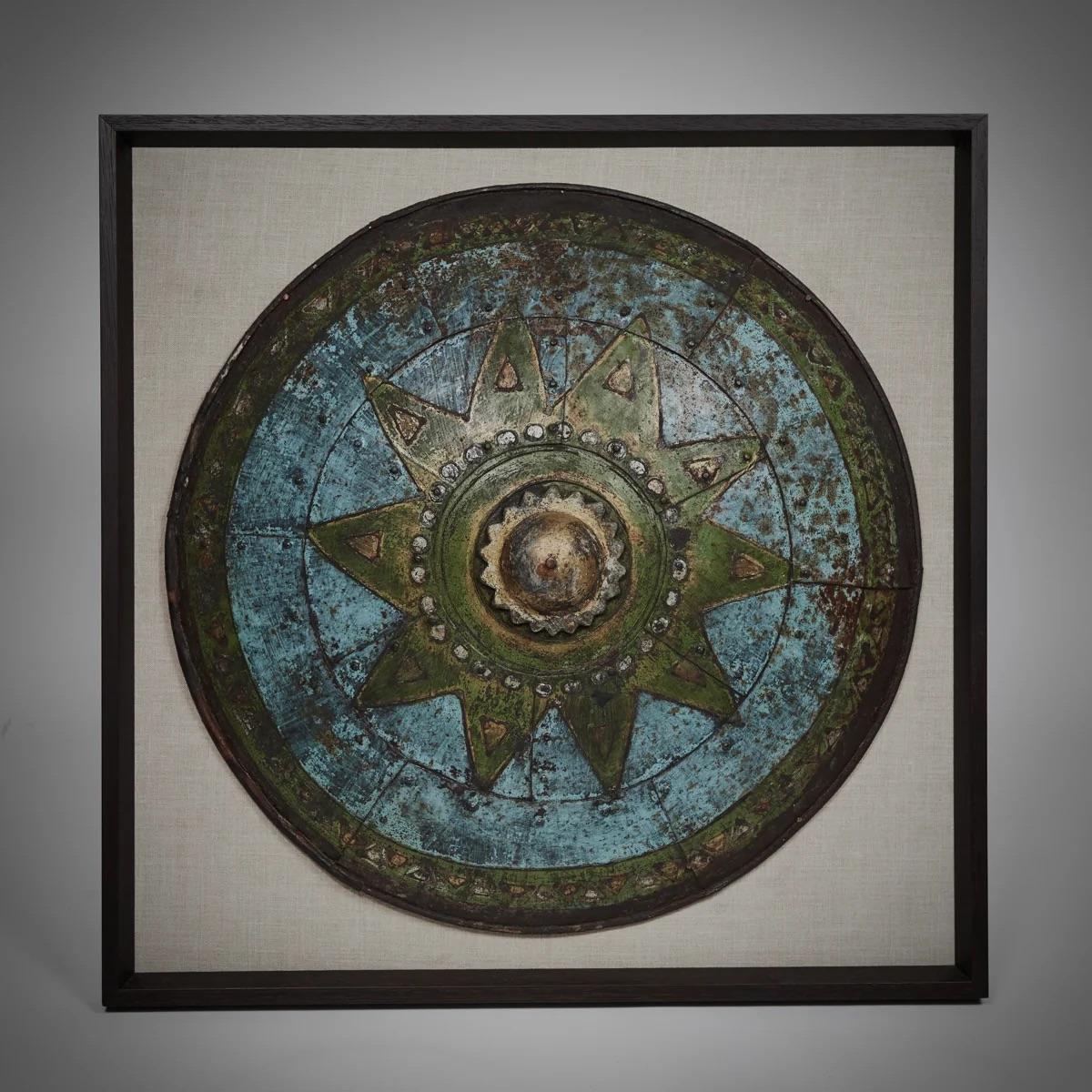 Questo scudo di scena unico, una reliquia dei famosi Pinewood Studios di Londra, è incorniciato da un elegante bordo nero e montato su uno sfondo di lino color lino. Lo scudo stesso mostra una patina ipnotica, ogni segno e cambiamento di colore