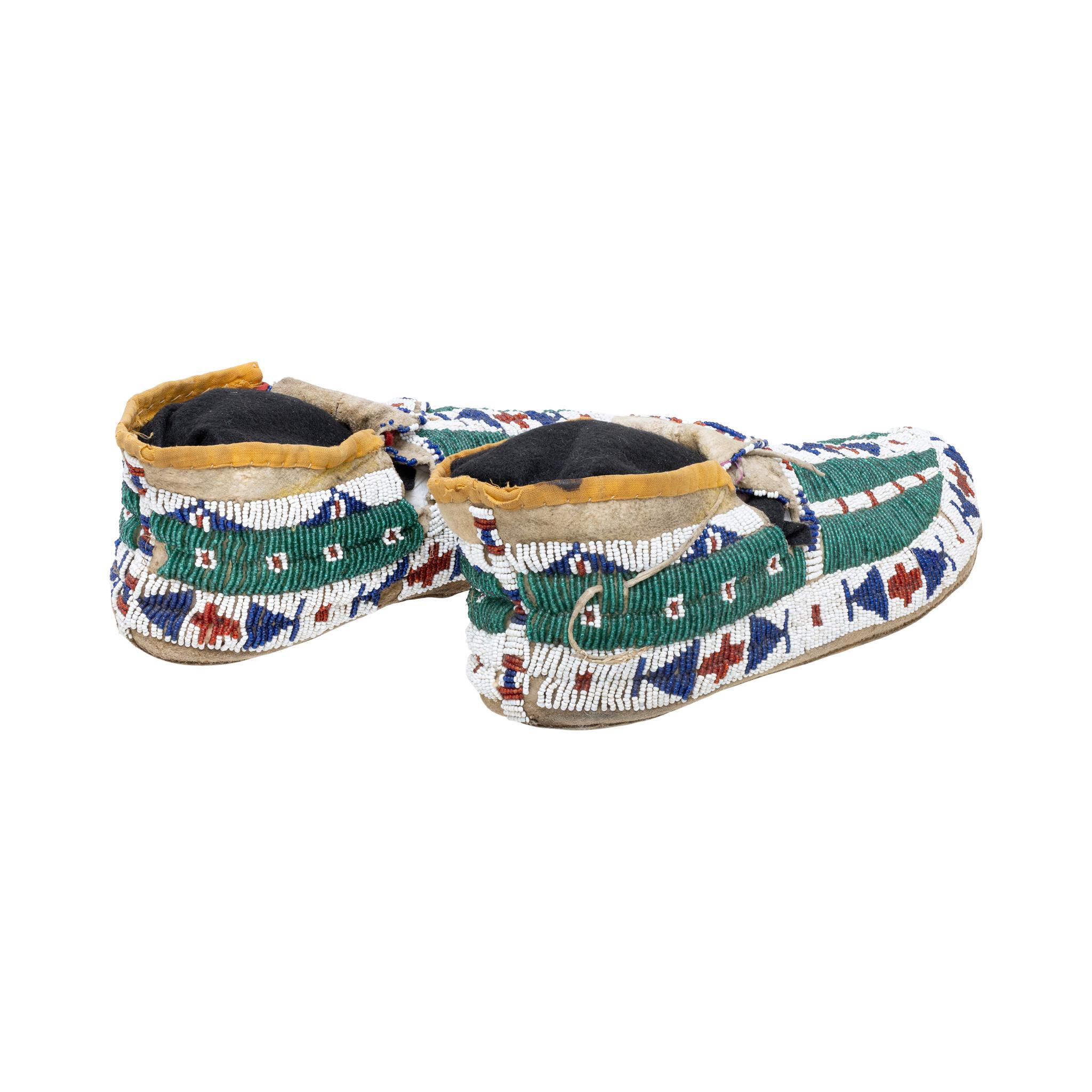 Native American Sioux Indian beaded moccasins with buffalo hoof design, beaded tabs and parfleche soles. Stunning geometric beaded designs done in colors of green, red, blue, and white. Would display nicely in a handmade indigenous beadwork