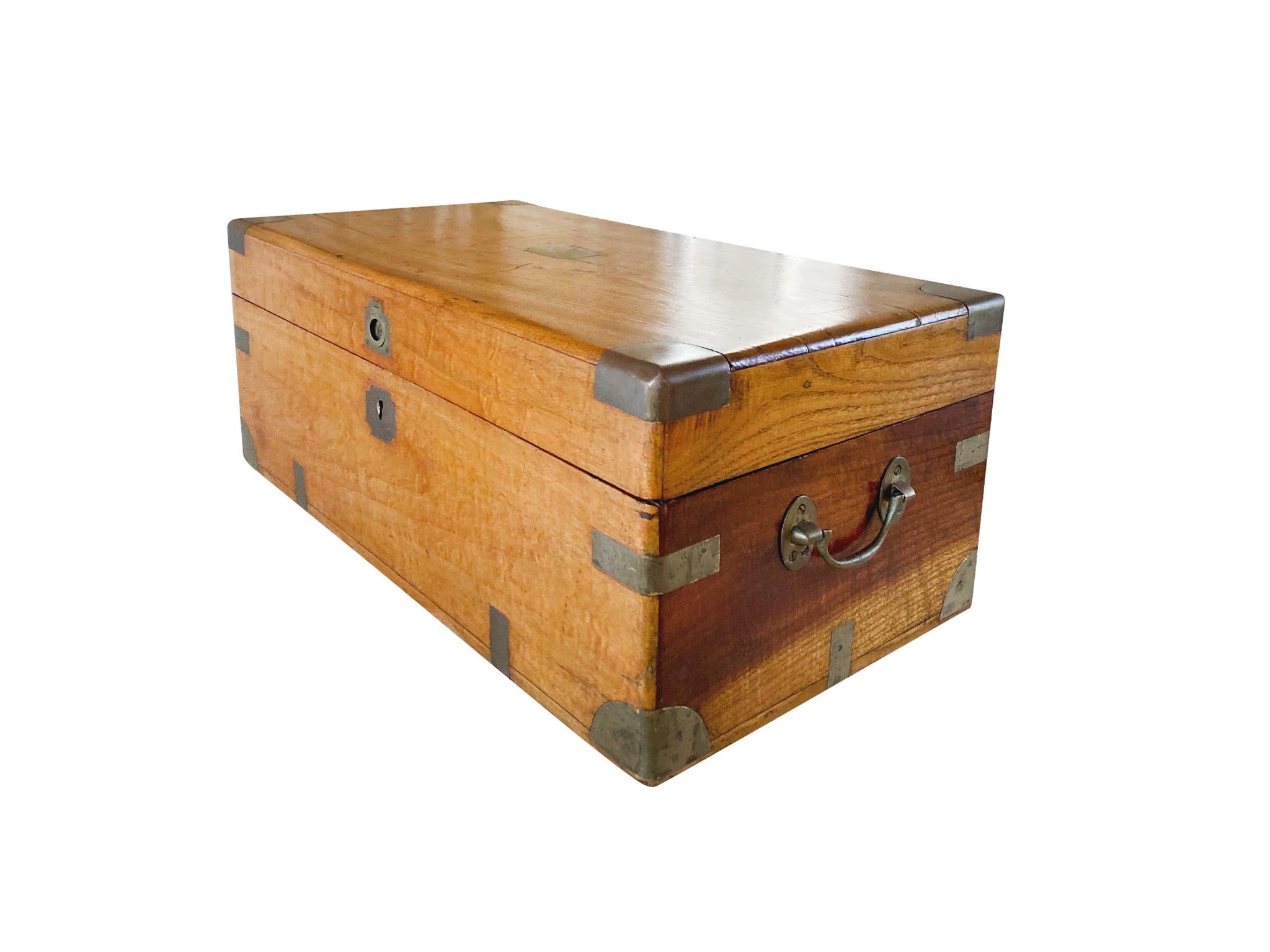 This small camphorwood chest was hand-crafted in the Early 20th Century. It is constructed with brass trims on the corners and edges, and bail handles mounted to the sides. The wood is smooth, and warm-toned, with light-dark variations in the