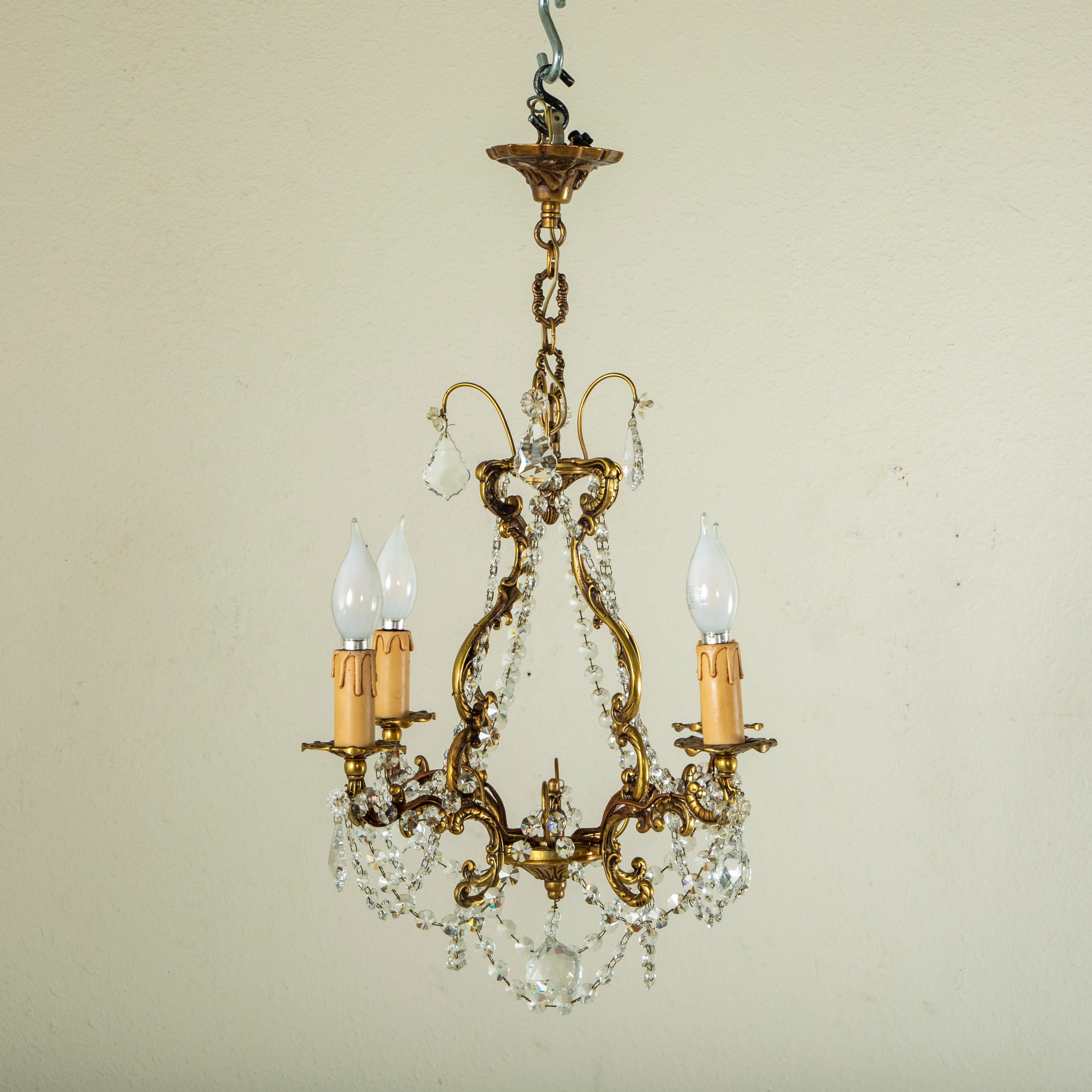 This small scale bronze chandelier features gadrooned strands of Strass crystals and four elegantly curved arms detailed with Strass crystal pendaloques. Each arm is fitted with a bronze bobeche that sits at the base of each of its four faux candle