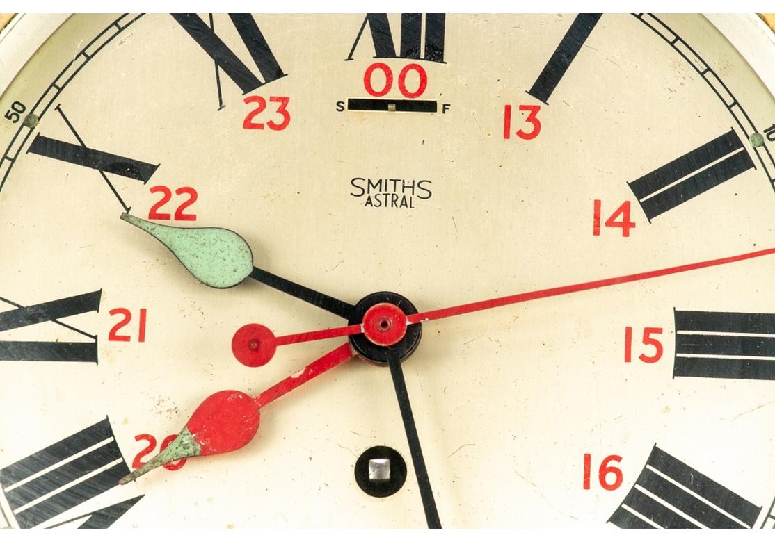 Early 20th century Smiths Astral [Great Britain] shipboard brass clock, circa 1930. A brass case with inset beveled glass panel that reveals a silvertone clock face with black enamel Roman numerals and red enamel Arabic numeral seconds. Four hands