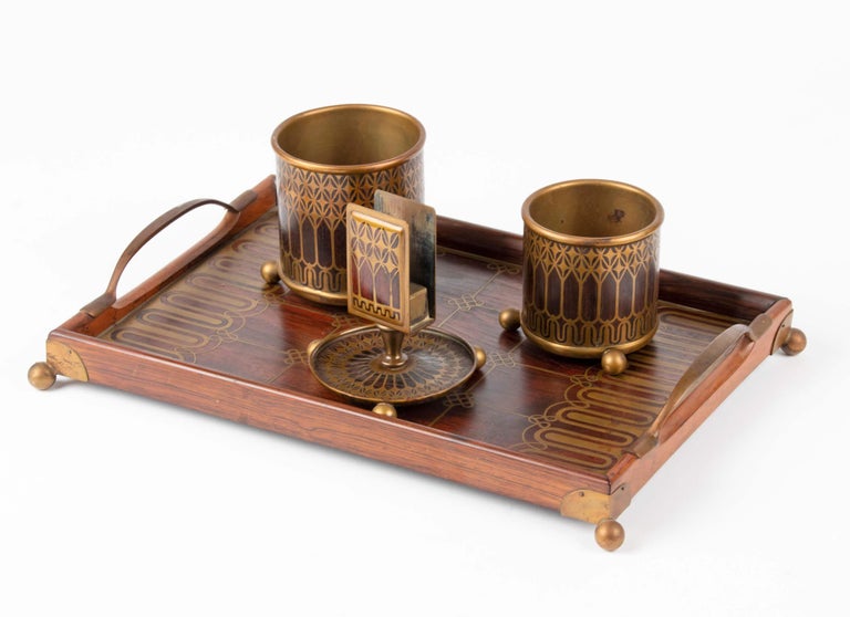A refined smoking set in Art Nouveau style. Made of solid rosewood with brass inlay. Consisting of a tray, two cups for cigarettes and a match holder. It is signed on the bottom of the tray, Erhard & Sohn, Germany around 1900-1905. 
Erhard & Söhne