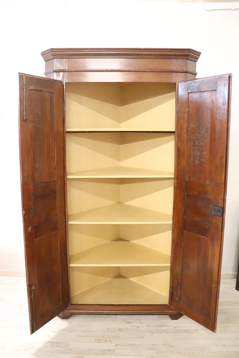 Early 20th century Italian antique corner cupboard. High quality furniture in solid walnut wood. The wood has a beautiful light color. Featuring two doors on the front. Internally equipped with four shelves. Interior lined with elegant yellow