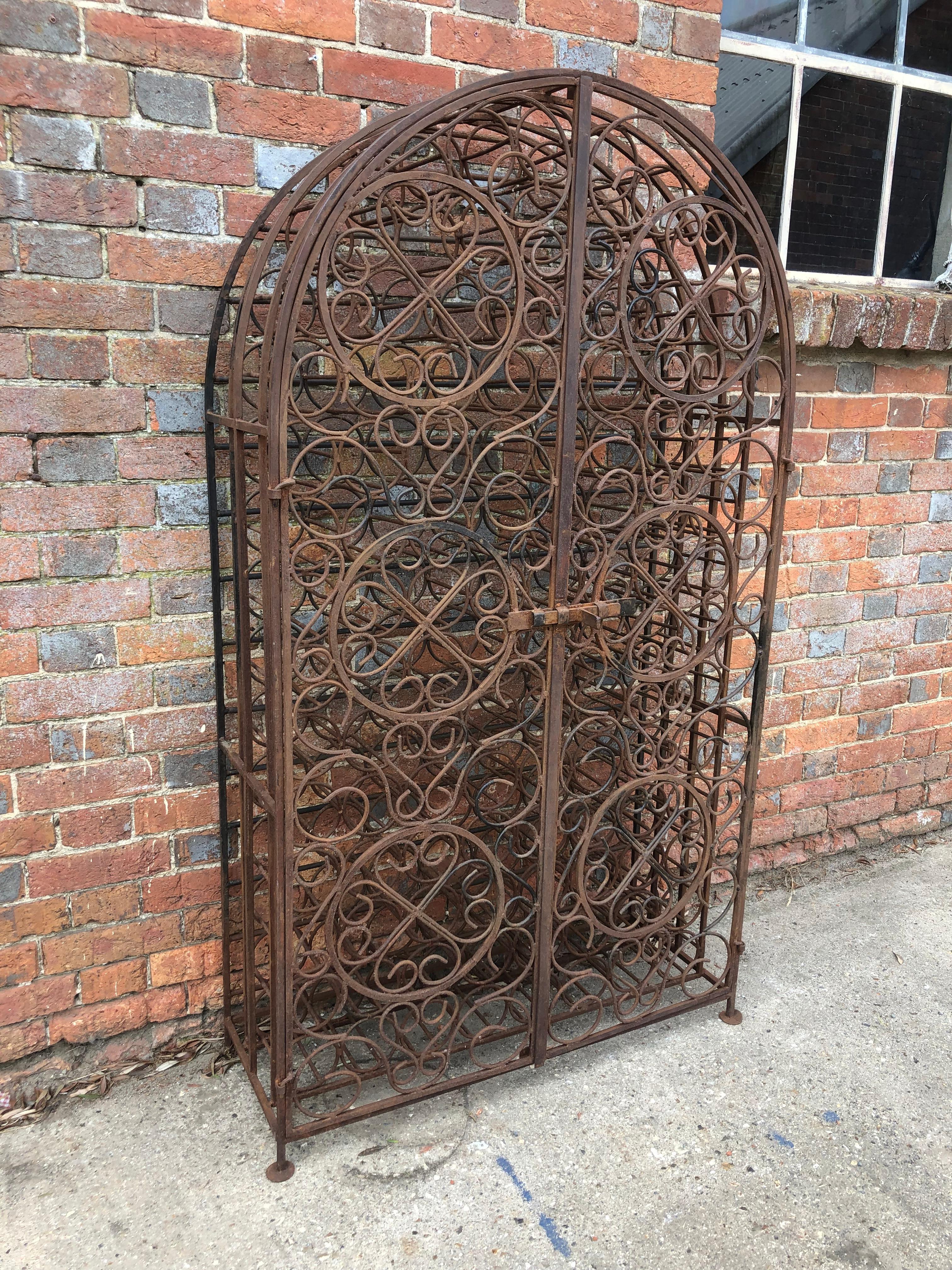 A wonderfully ornate and rustic French iron wine rack with two doors and a sliding lock and space for 107 wine or champagne bottles.