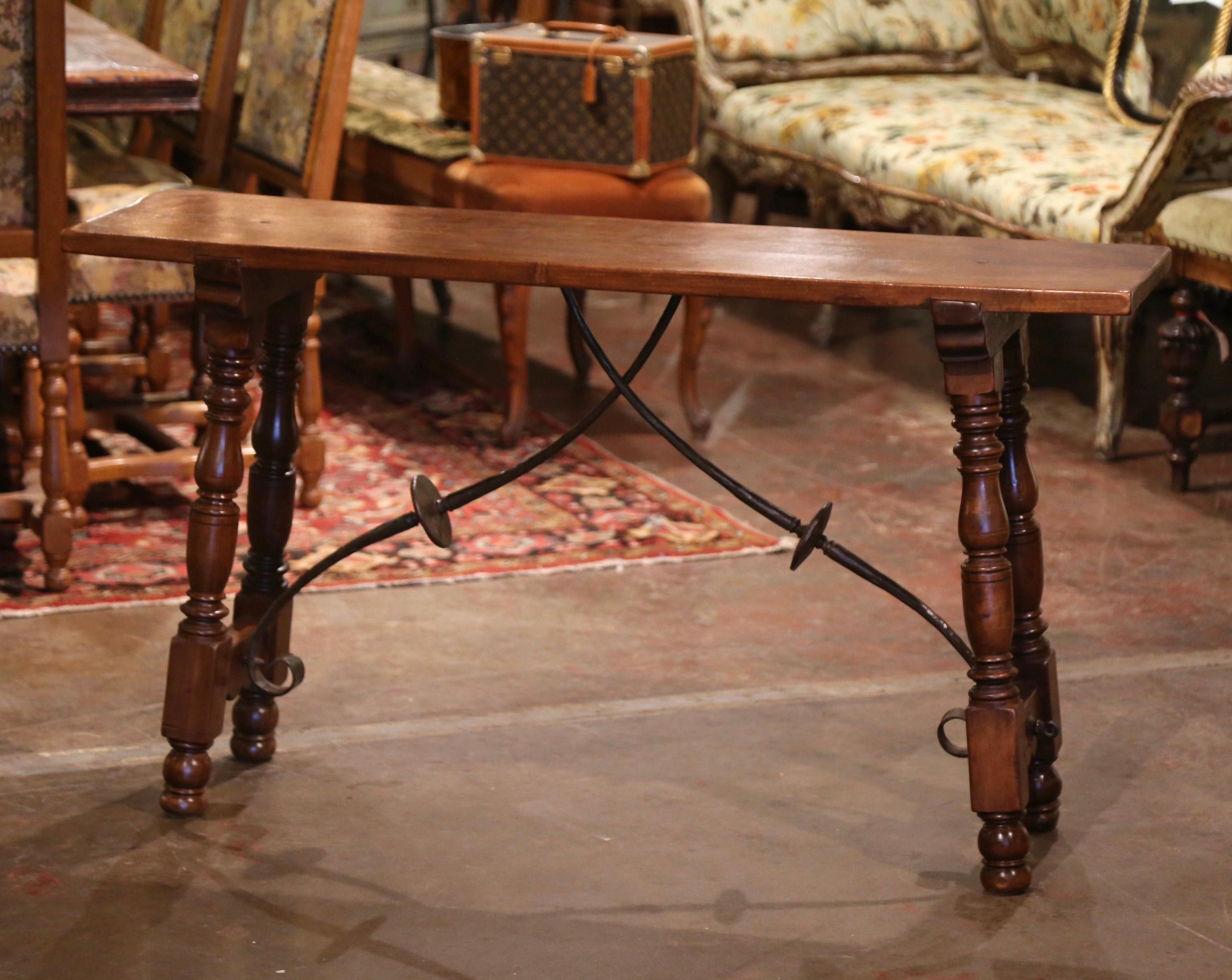 Place this elegant antique console table behind a sofa. Carved in Spain circa 1920, the narrow trestle table stands on two intricate carved turned legs, connected with a thick scrolled forged foliate iron stretcher. The table is in excellent