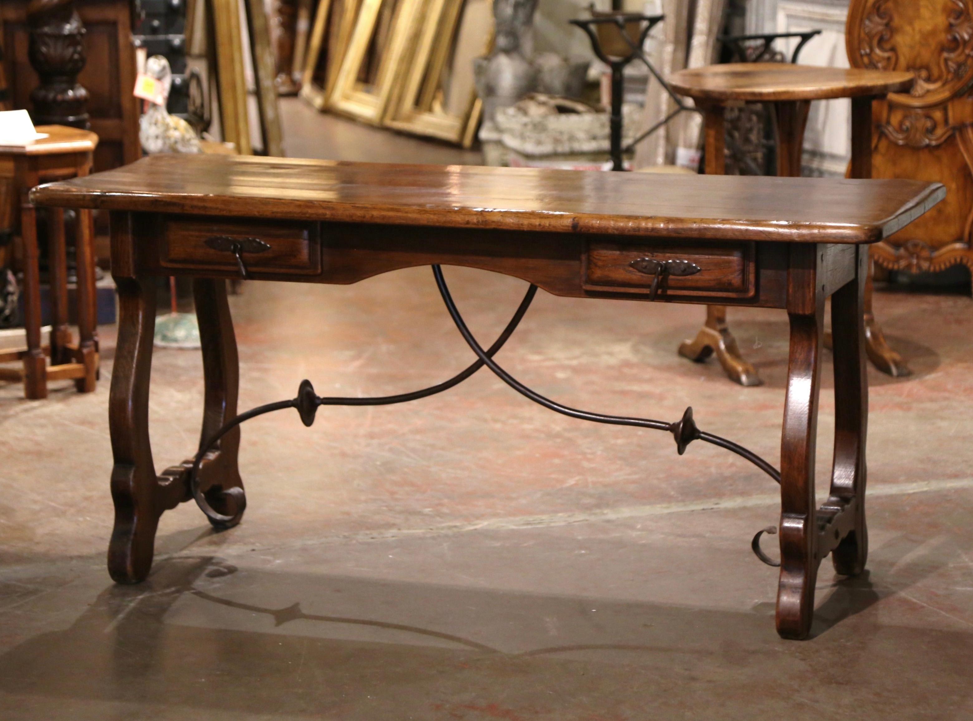 Add an elegant focal point to your study or library with this antique table desk. Carved in Spain circa 1920, the trestle table stands on two intricate curved legs connected with a thick forged wrought iron stretcher. The 6 foot desk features two