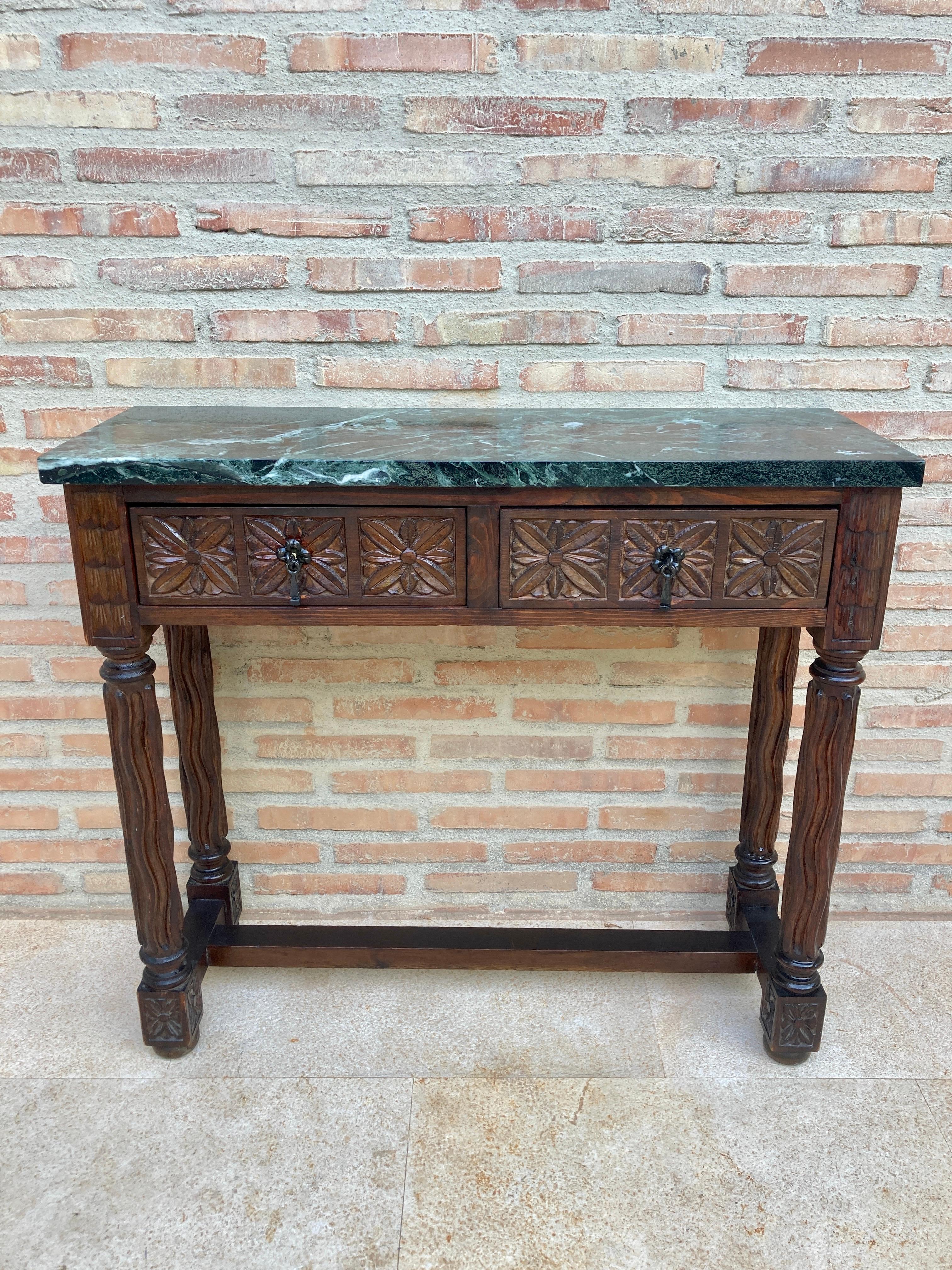 Early 20th century Spanish carved walnut console table with two drawers and green marble top.
This early 20th century Spanish Console table has two carved drawers with black wrought iron handles and Solomonic hand carved twist legs joined by a