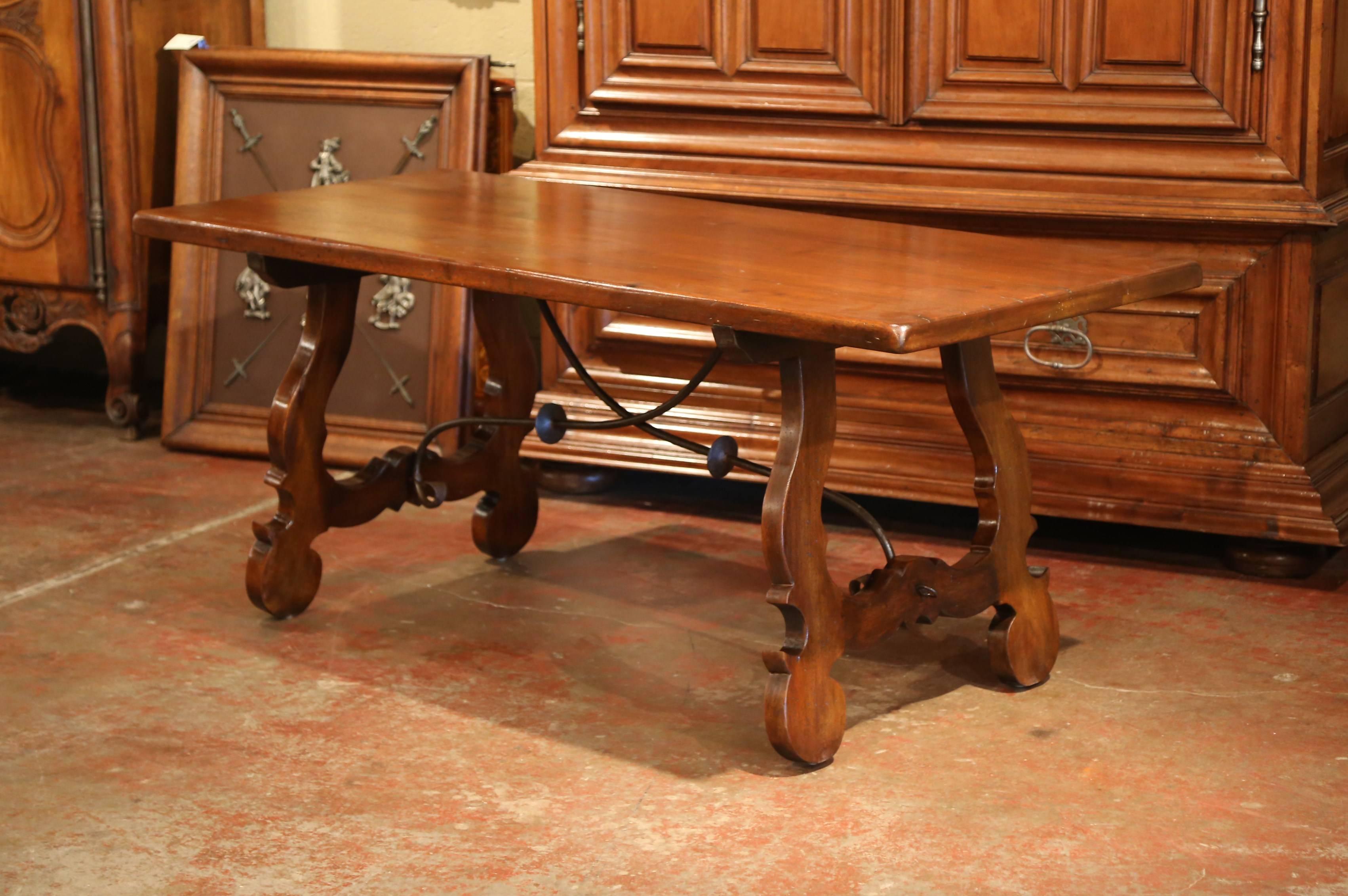 Elegant antique fruitwood farm table from Spain; crafted circa 1920, the trestle table features a rectangular top over two carved and shaped lyre-form legs joined by forged iron stretcher. The table is in excellent condition with a rich walnut