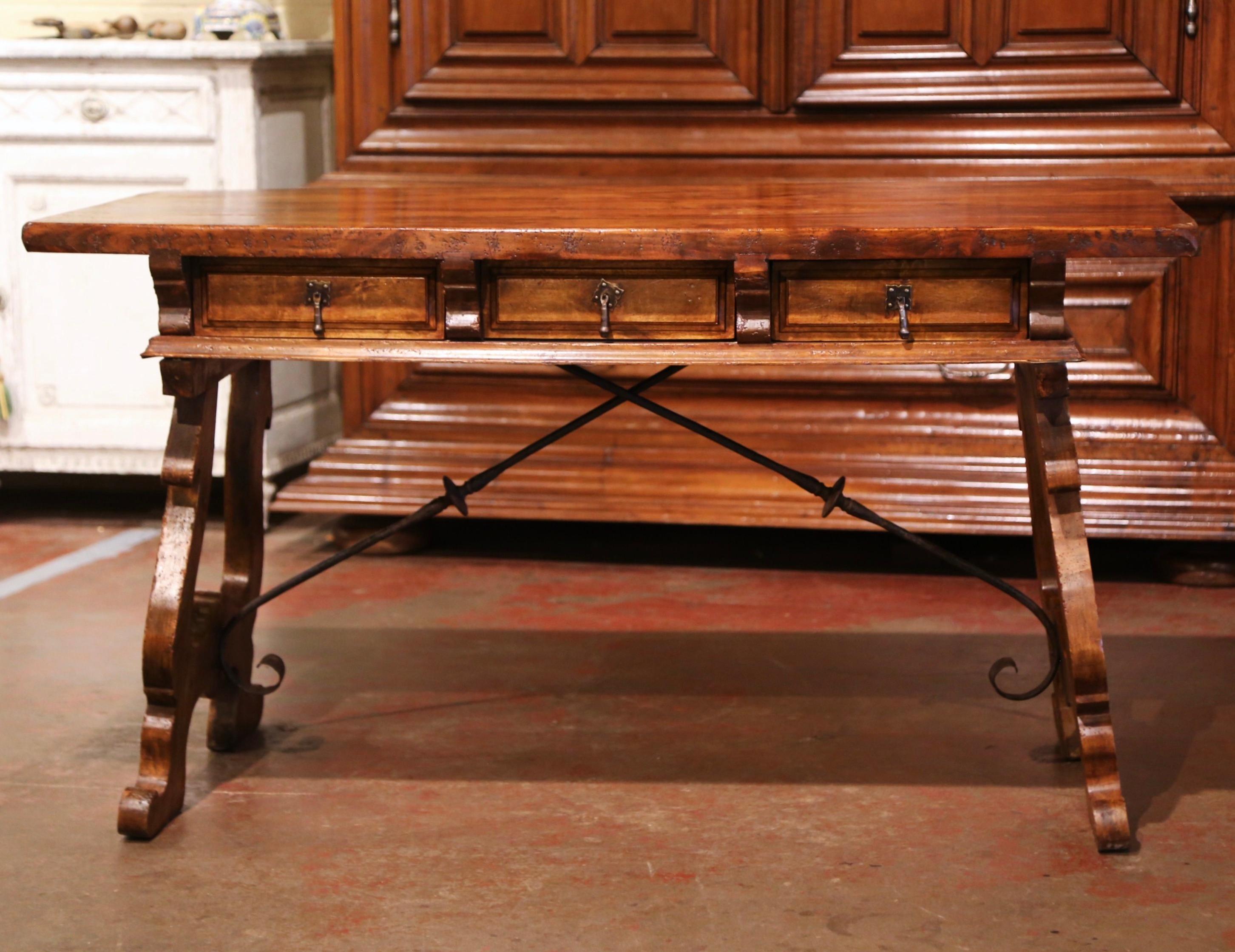 Add an elegant focal point to your study or library with this antique fruitwood desk. Carved in Spain circa 1920, the trestle table stands on two intricate carved legs connected with a thick forged iron stretcher. The rectangular desk features three