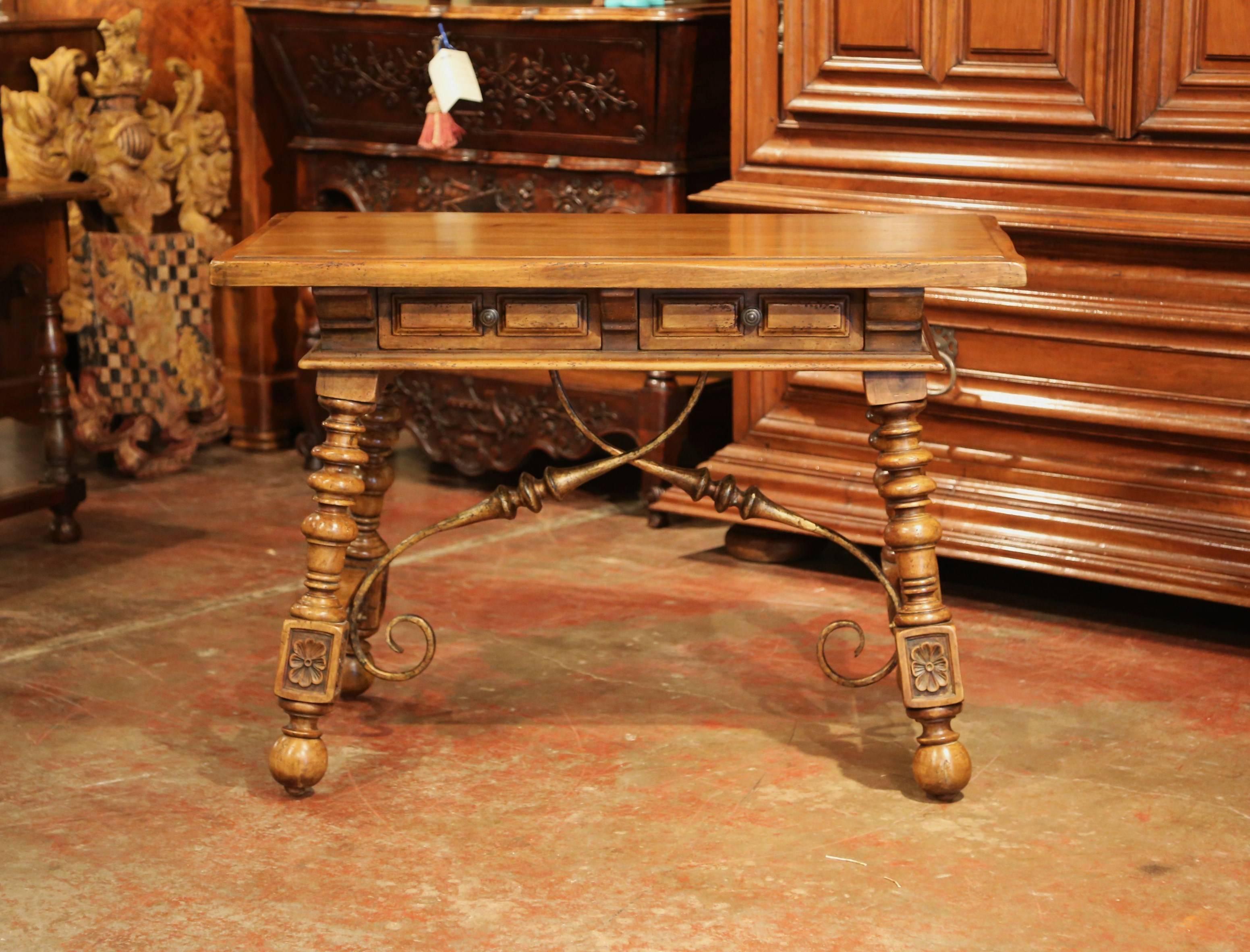Complete your study or library with this beautifully carved, fruitwood table desk. Crafted in Spain, circa 1920, the small writing table stands on four turned legs connected with a wrought iron stretcher. All four sides with two front drawers, have
