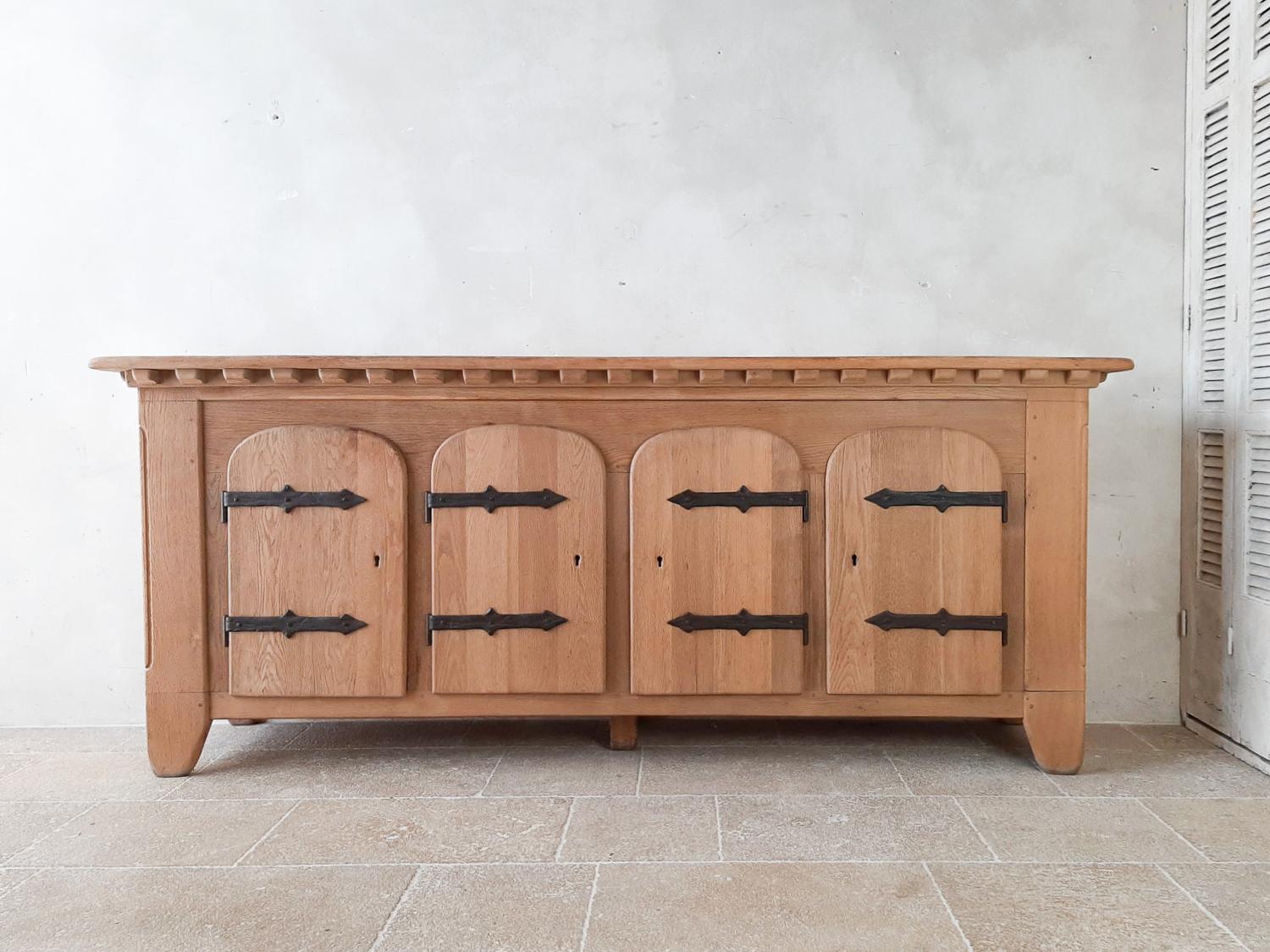 Mid 20th Century Spanish Oak credenza from the 1940s. Stunning solid oak sideboard with typical arched doors and large wrought iron hinges. With wood pattern underneath the top all the way around the front and sides. The three left doors have a