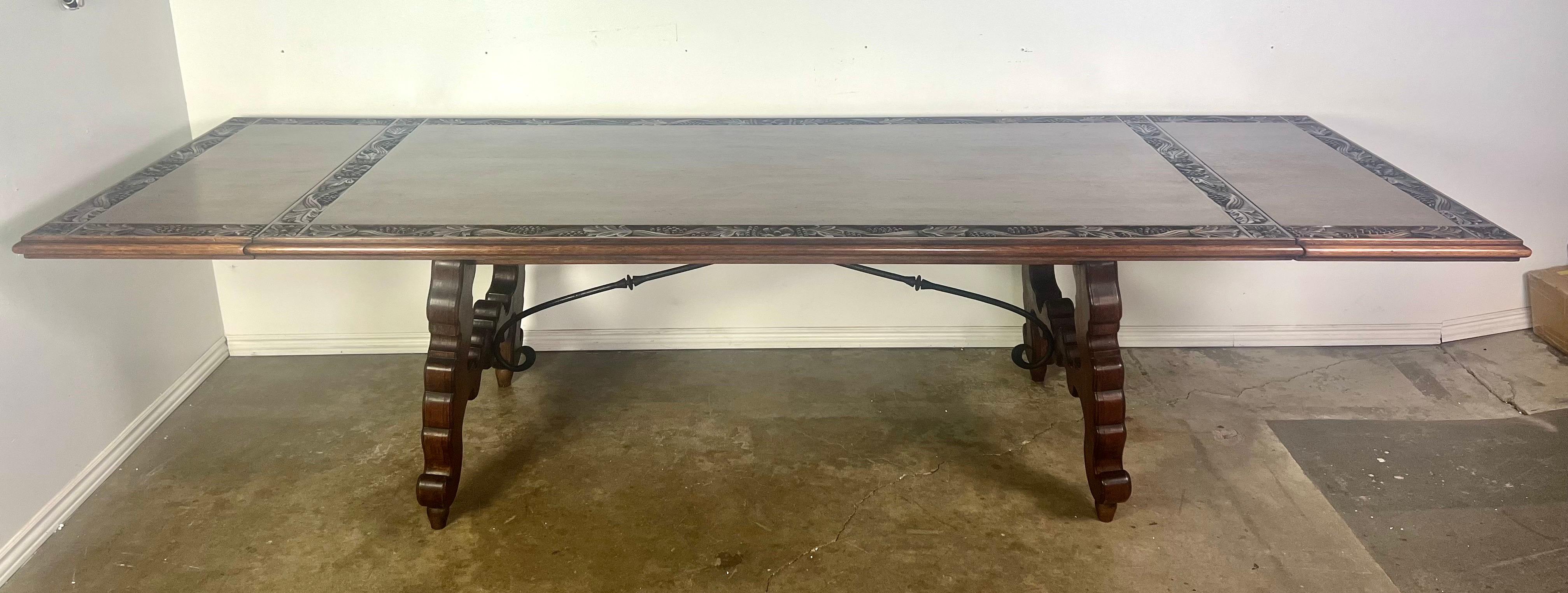 Early 20th Century Spanish refractory table with hand carved grapevines around the perimeter of the table.  There are two extensions on either end that are easy to remove.  This walnut table and an iron stretcher at it's base and stands on two lyre