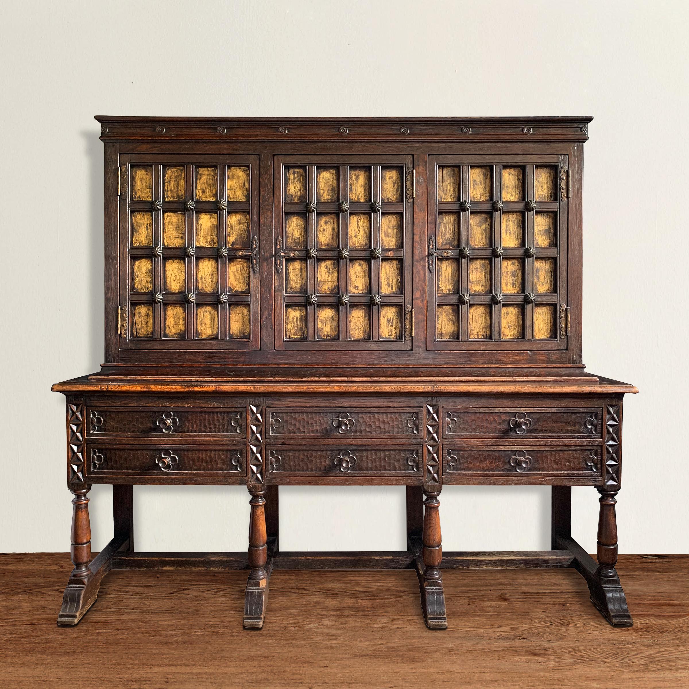 A wonderful early 20th century English Tudor Revival oak cabinet with three doors, each with raised lattice frames with heavy iron nail heads, backed with gold leaf panels, and retaining their original locks and keys. Six drawers below with chip