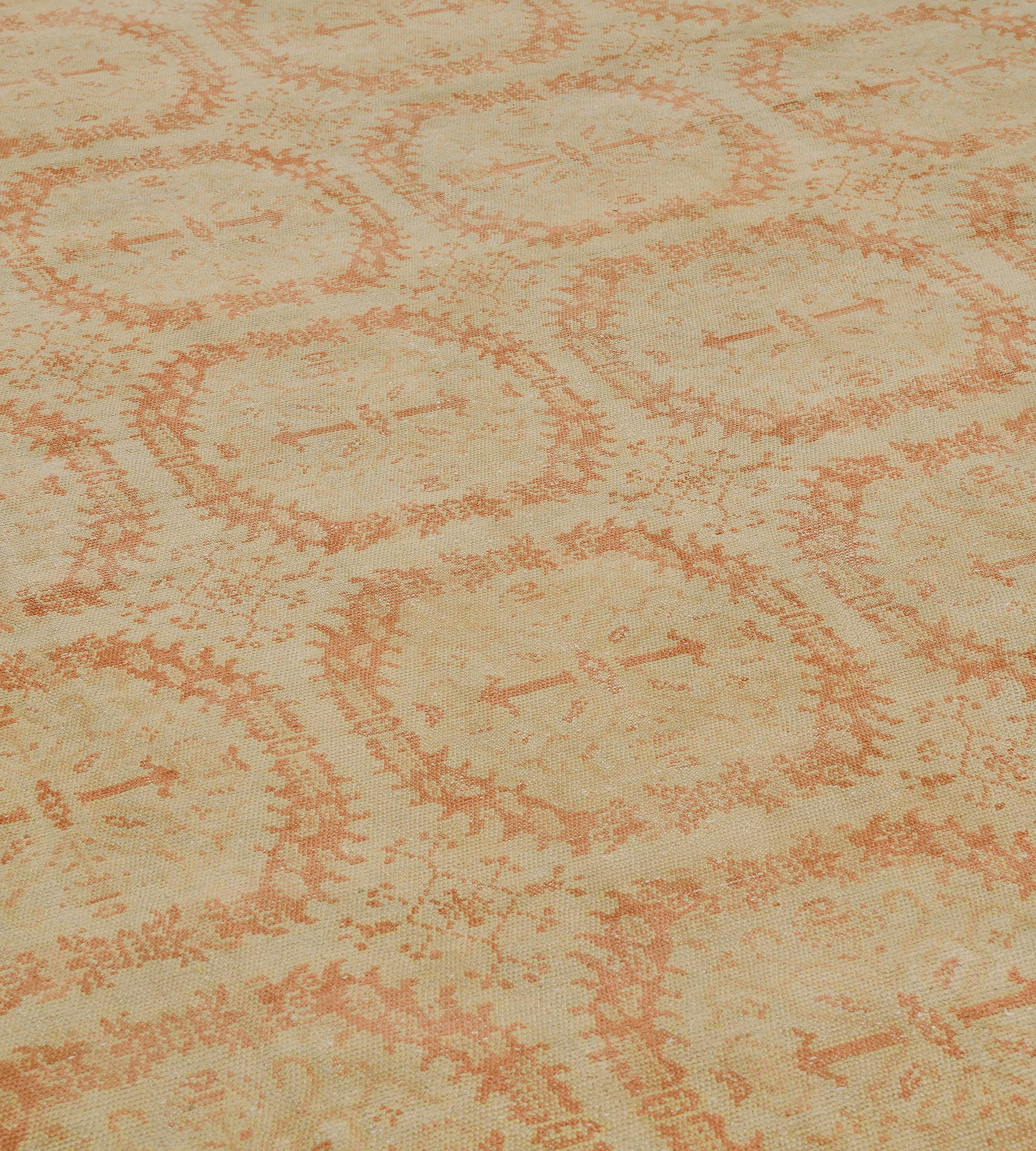 This traditional handwoven Spanish rug has an overall sandy beige field of rust floral wreaths forming lattice, each enclosing radiating floral motif and separated by delicate lozenges, in a complementary beige border of stylized linked palmettes,