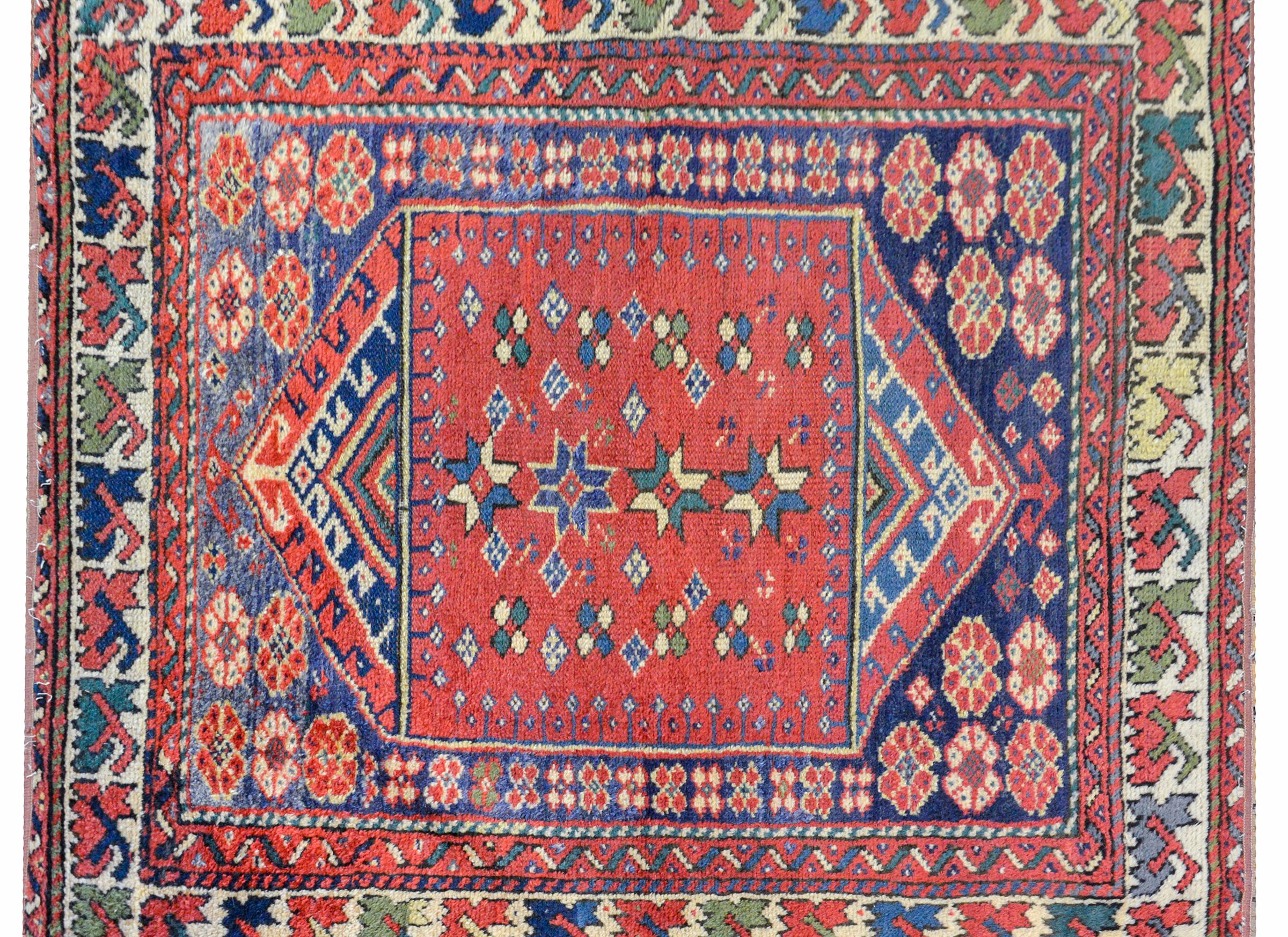 A sweet early 20th century Turkish Sparta rug with a wonderful tribal pattern containing stylized flowers woven in indigo, green, and gold, on a crimson background, on another background with more flowers, and all surrounded by multiple borders