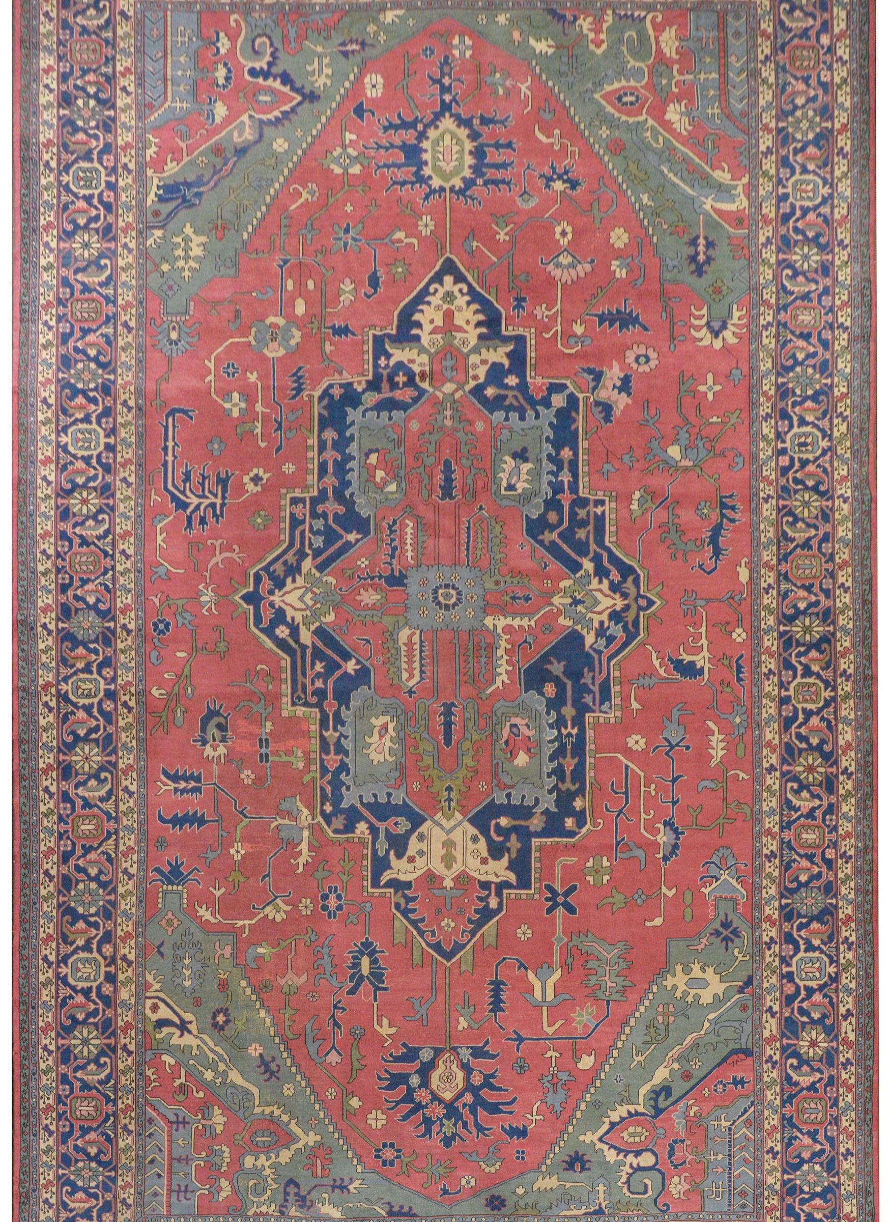 A wonderful massive early 20th century Turkish Sparta rug a traditional Serapi pattern containing a large central oblong floral medallion woven in muted crimson, light and dark indigo, green, and gold, all on a muted crimson field of myriad flowers