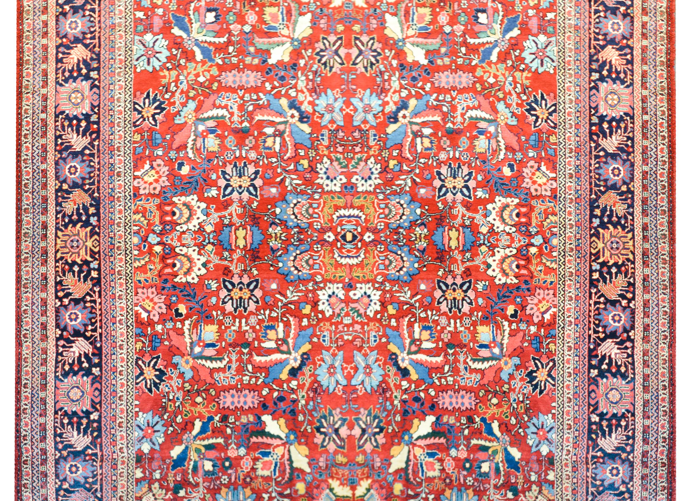 An outstanding early 20th century Mahal rug with an all-over mirrored floral pattern woven in bold colors including pink, light and dark indigo, and white, set against a dark crimson background, and surrounded by a wide border with a large-scale