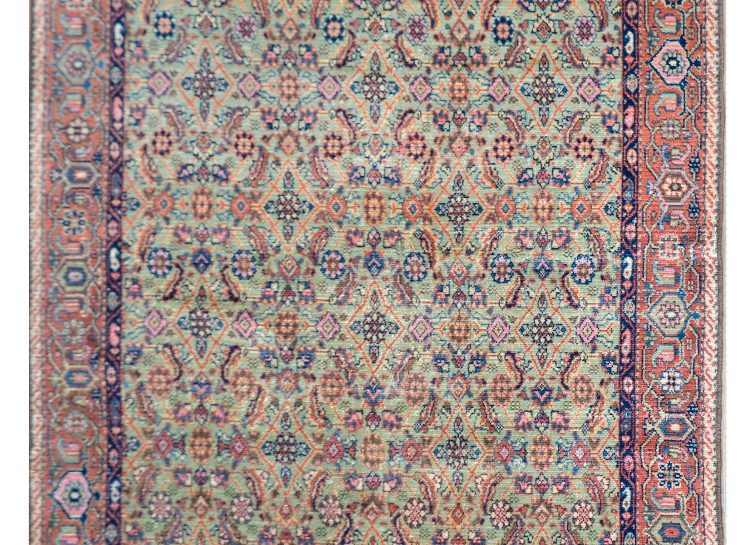A beautiful early 20th century Persian Sultanabad rug with an all-over trellis floral and leaf pattern woven in orange, gold, pink, and indigo, against a pale green background, and surrounded by a simple border with a stylized floral pattern.