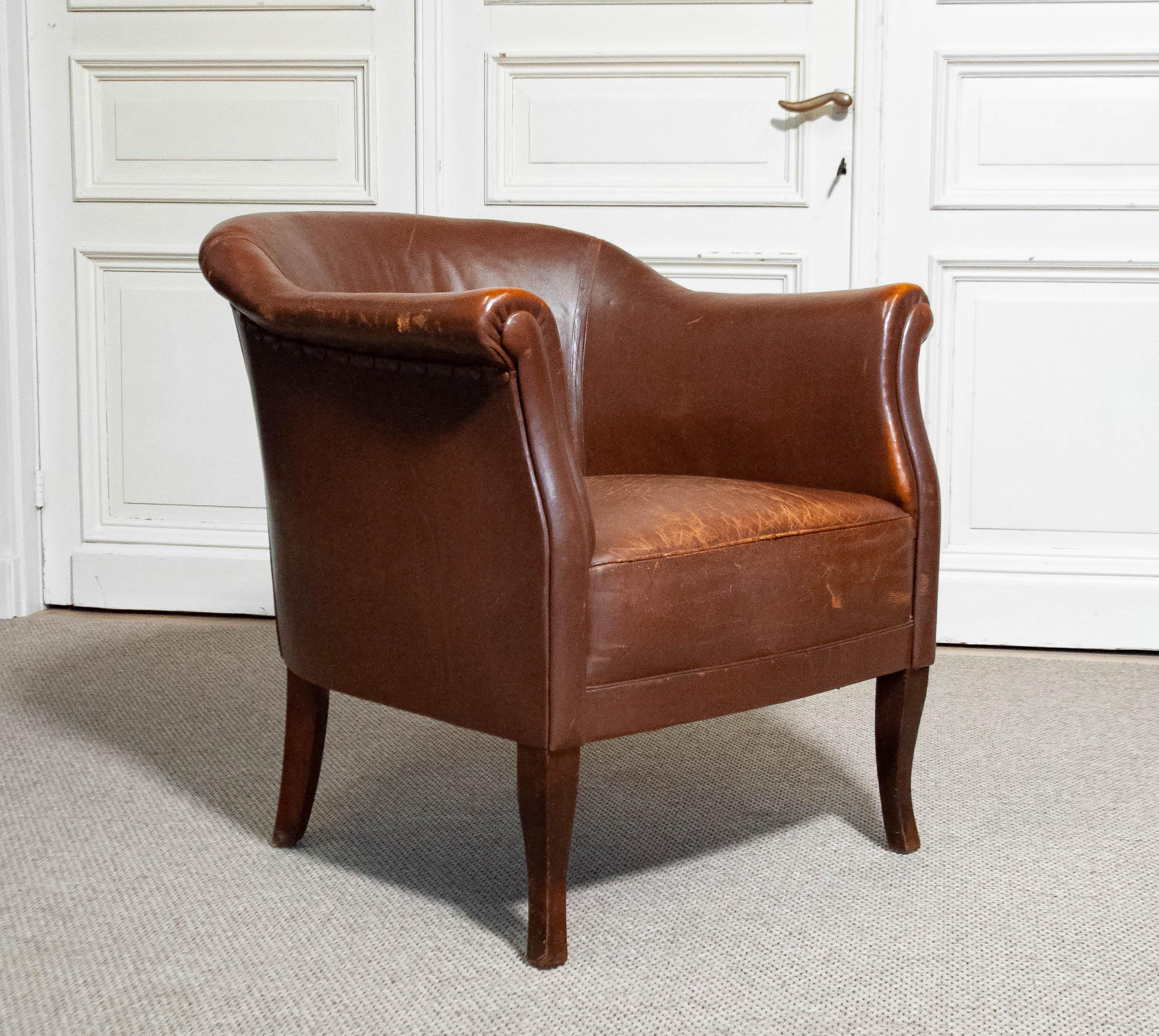 This early 20th-century Swedish Cigar Club Chair features a sleek and slender design, embodying timeless elegance and comfort. Upholstered in rich tan-brown leather, the chair showcases a beautifully aged patina that adds character and warmth. Its