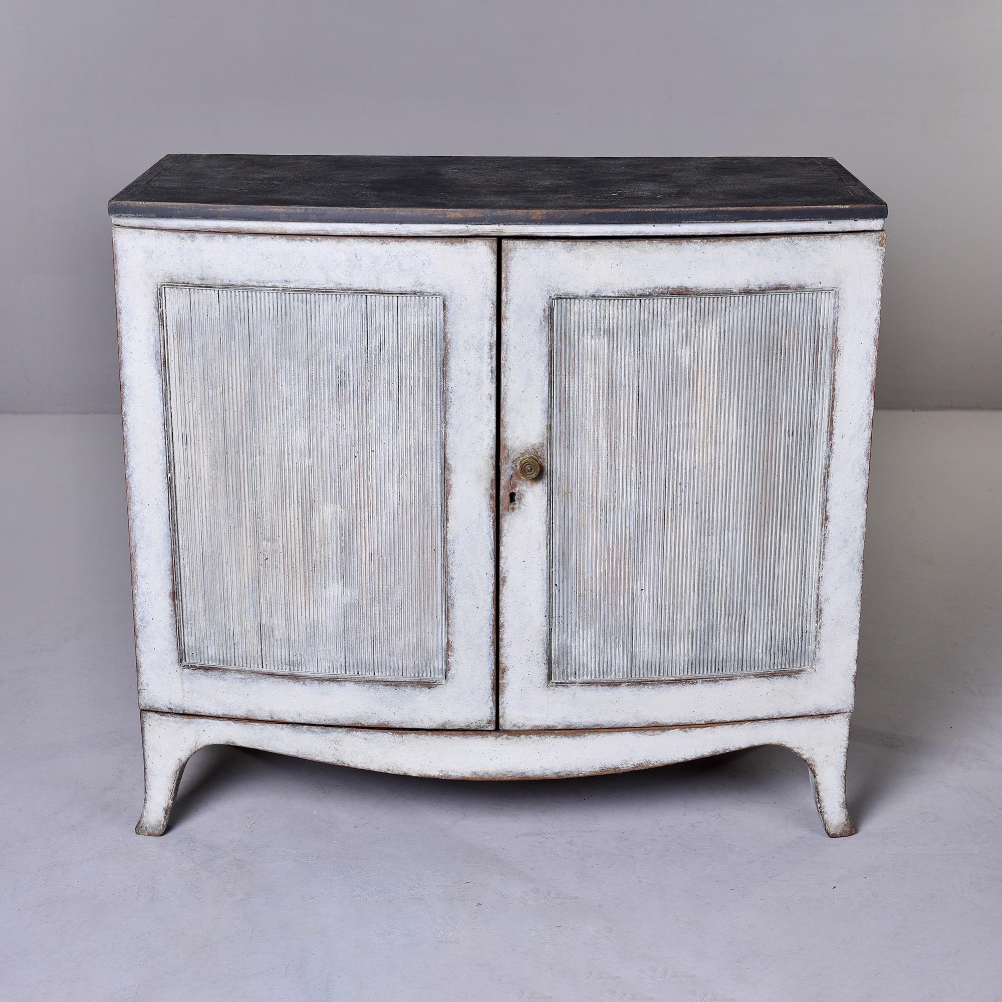 Found in England, this circa 1920s two door cabinet or chest has a soft black painted top with the rest of the cabinet finished in a contrasting soft white with gray undertone. Two hinged doors have reeded panels in the center and open to two fixed