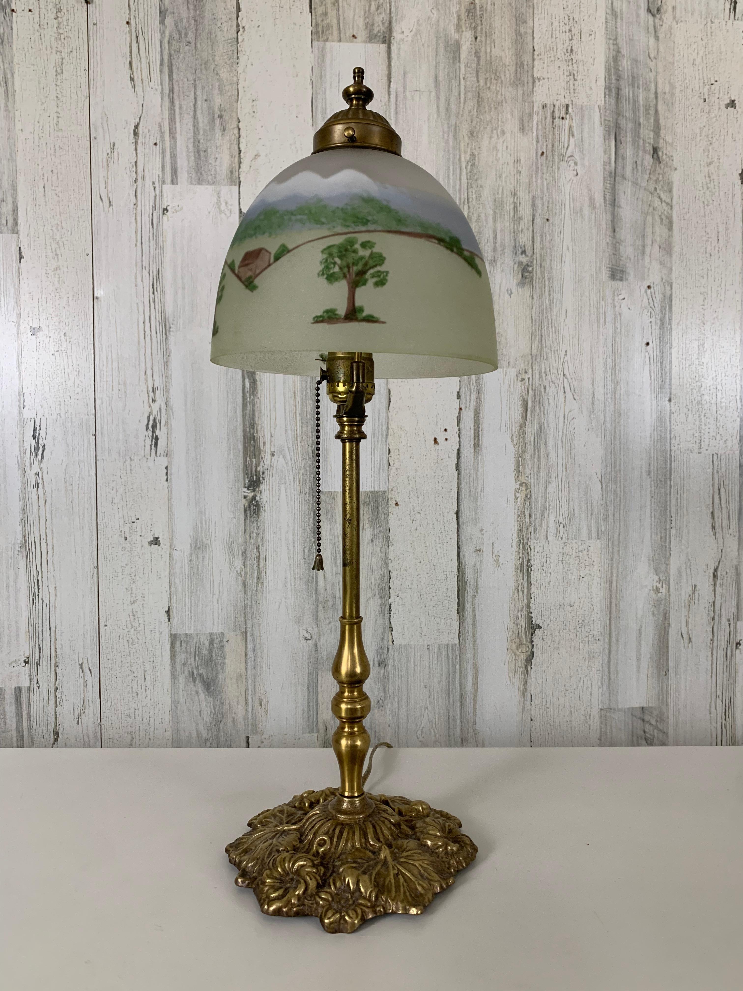 Lampe de table du début du 20e siècle avec abat-jour en forme de paysage peint à la main. Base à motif floral en laiton massif avec douille à chaîne.
