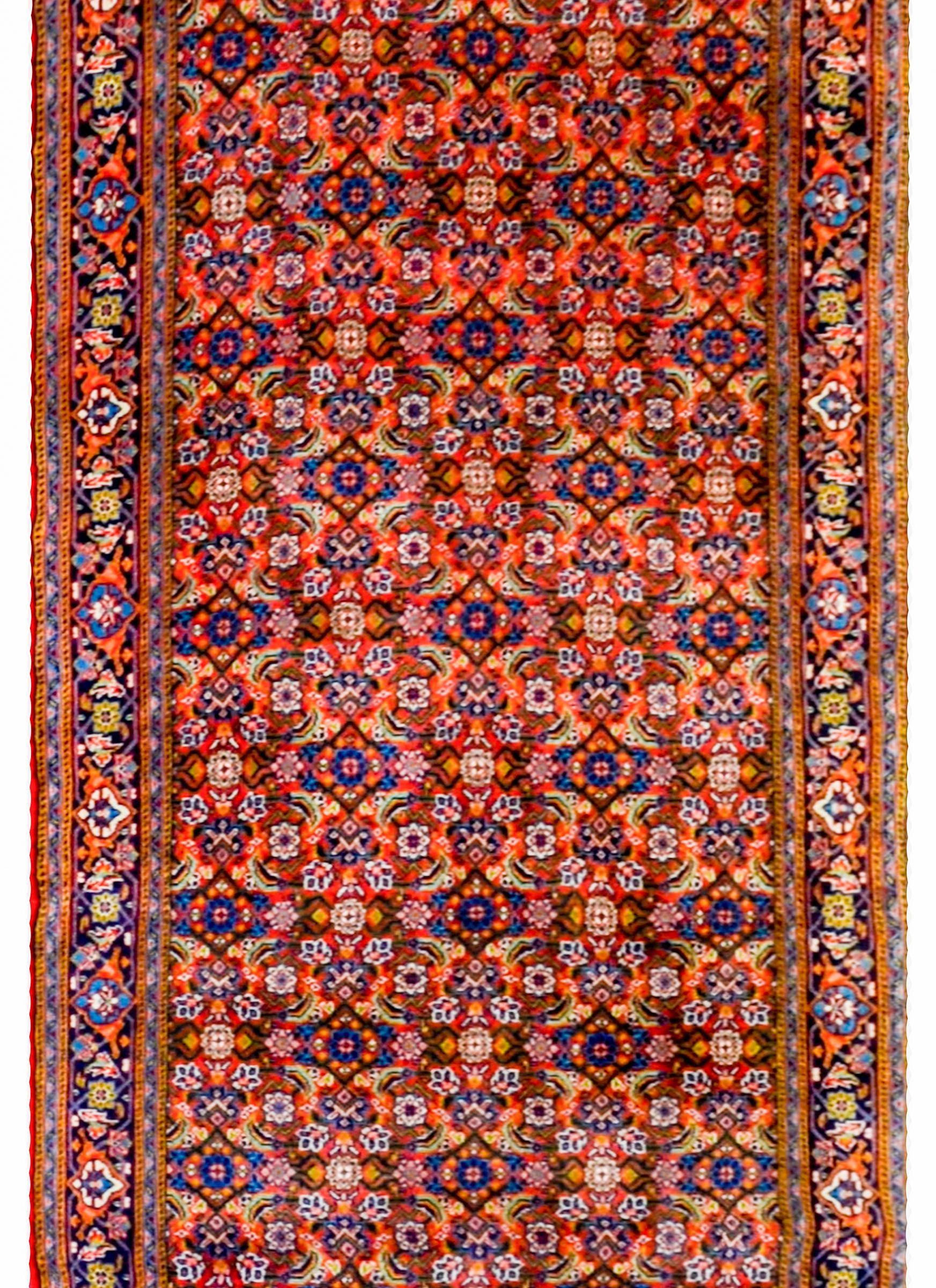 An early 20th century Persian Tabriz runner with a beautiful all-over lattice and floral pattern woven in indigo, pink, green, and gold, on a crimson background. The border is simple, with a wide central floral patterned stripe flanked by three