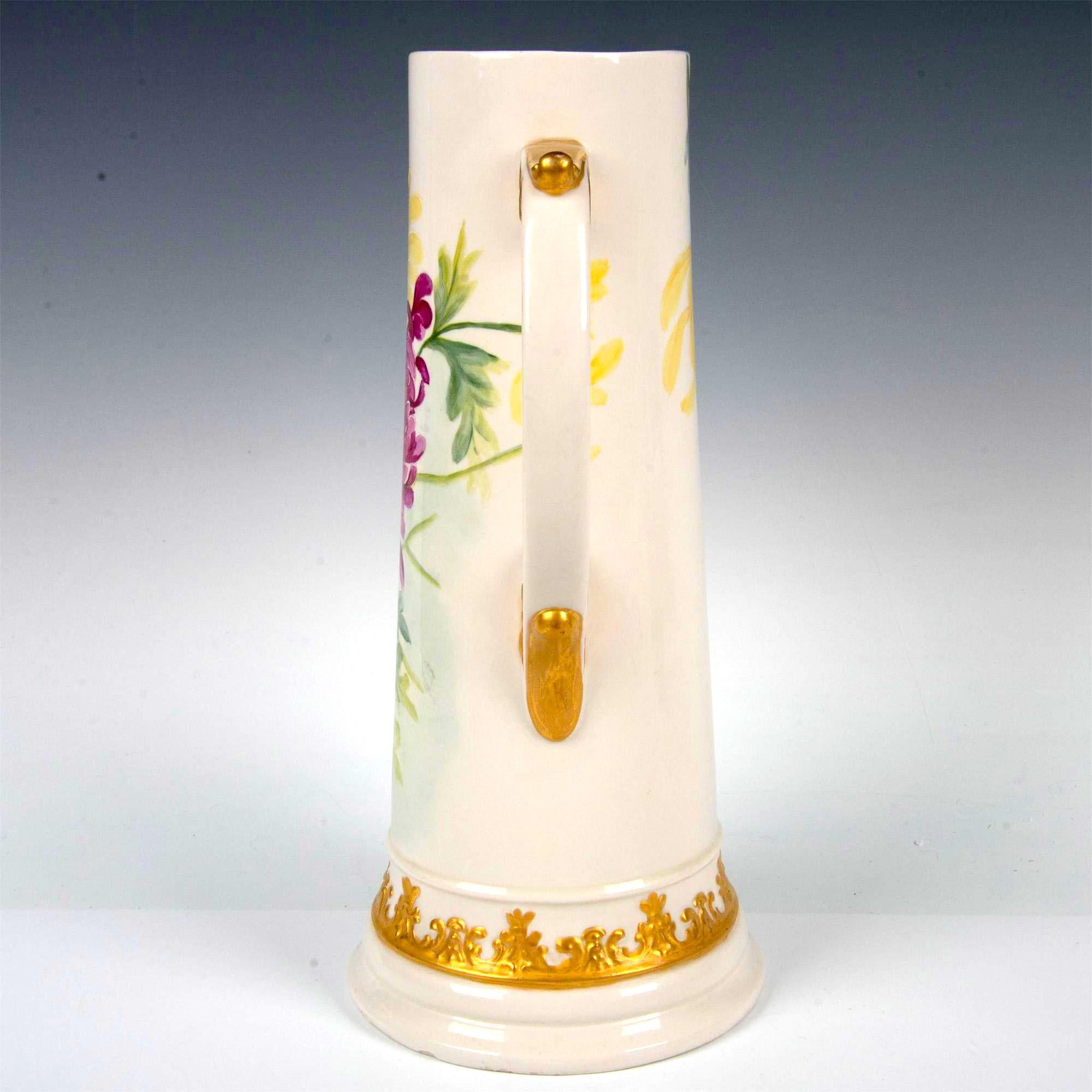 Experimenta la belleza y la elegancia de esta jarra de cerveza de porcelana blanca norteamericana de Belleek de principios del siglo XX. Esta impresionante pieza está meticulosamente elaborada y pintada a mano con vibrantes crisantemos fucsias y