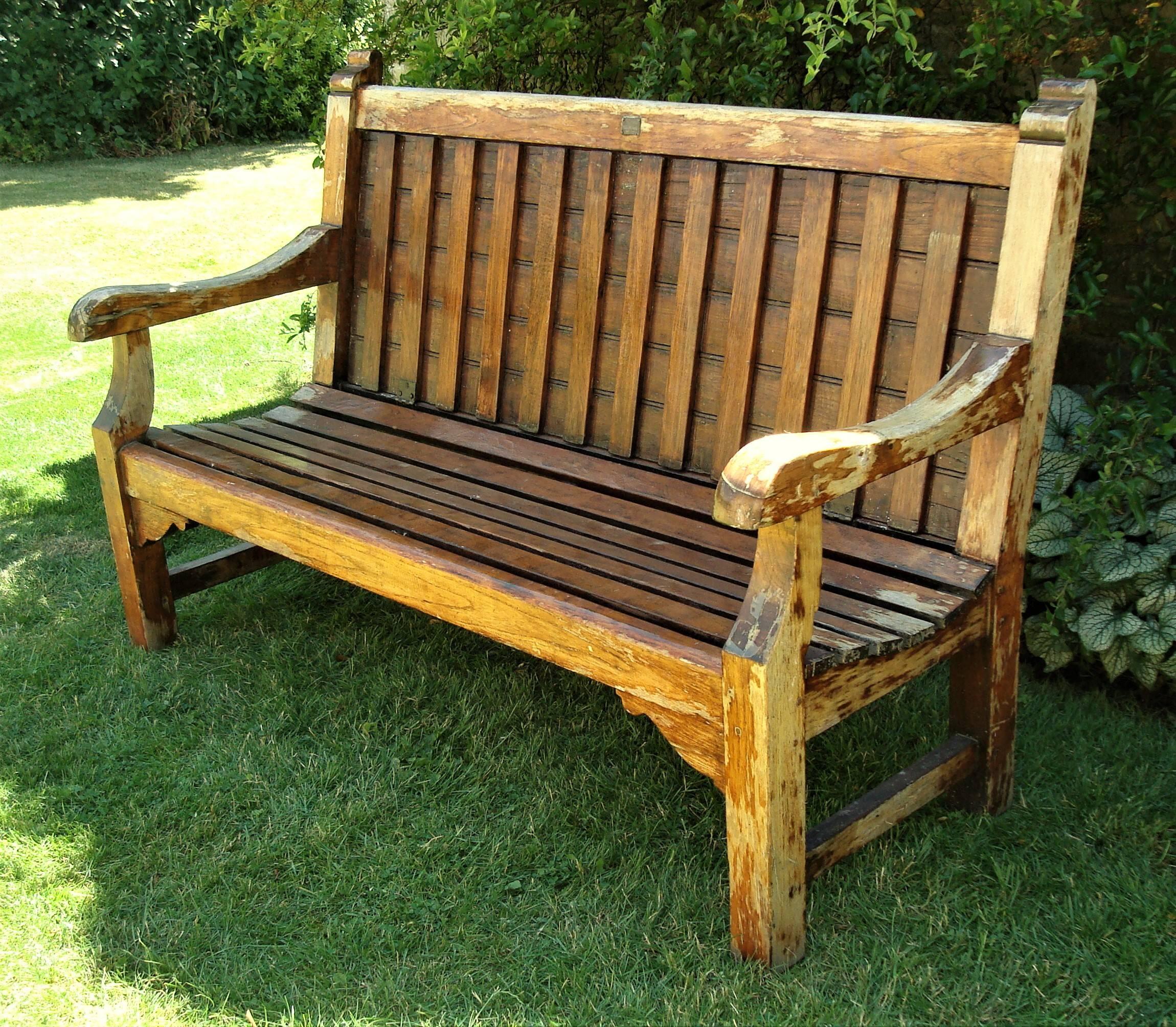 A rare early 20th century teak ship's bench, garden seat; having the very unusual feature of the inset slatted back being hinged to fold down, covering the seat, with the purpose of keeping the seat dry from rain or sea spray. The shaped arms