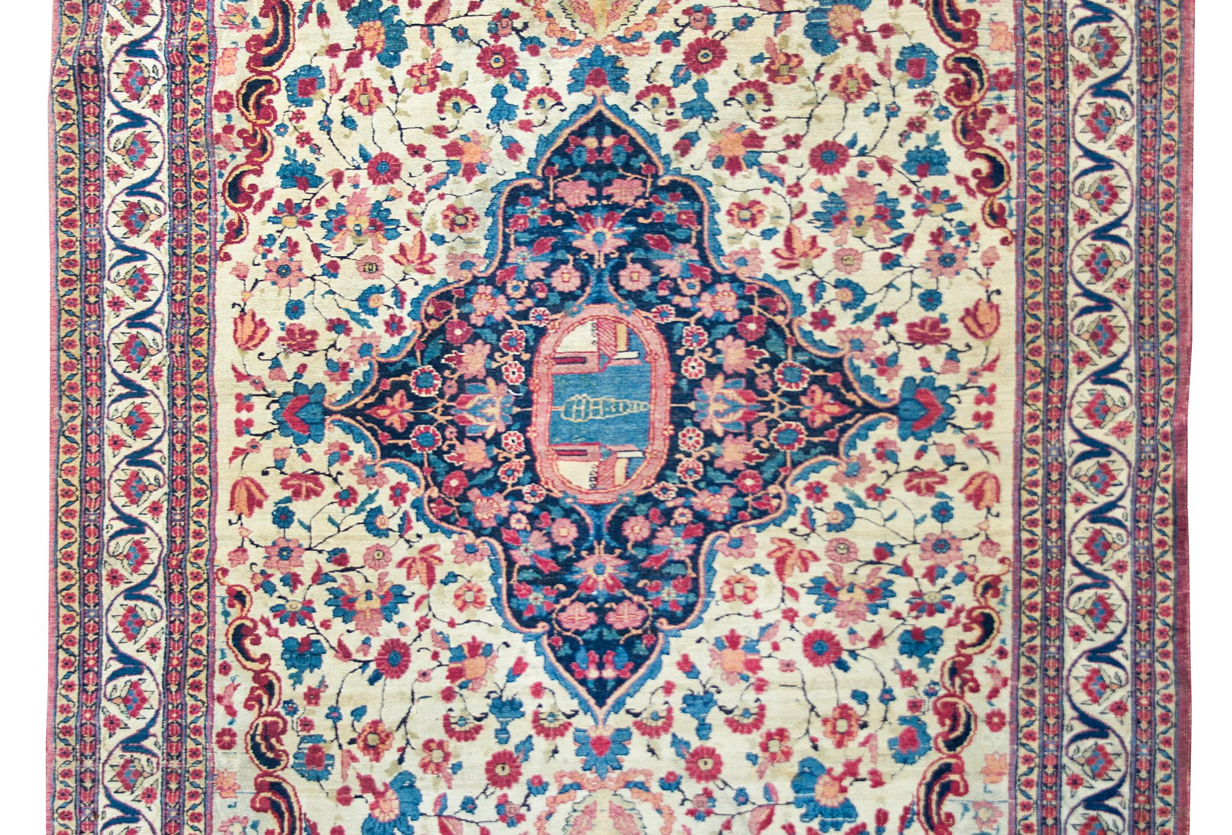 An incredible early 20th century Persian Tehran rug with a large central medallion with a single cypress tree between two buildings living amidst a field of flowers, and all surrounded by a wide border with more stylized flowers and scrolling vines,