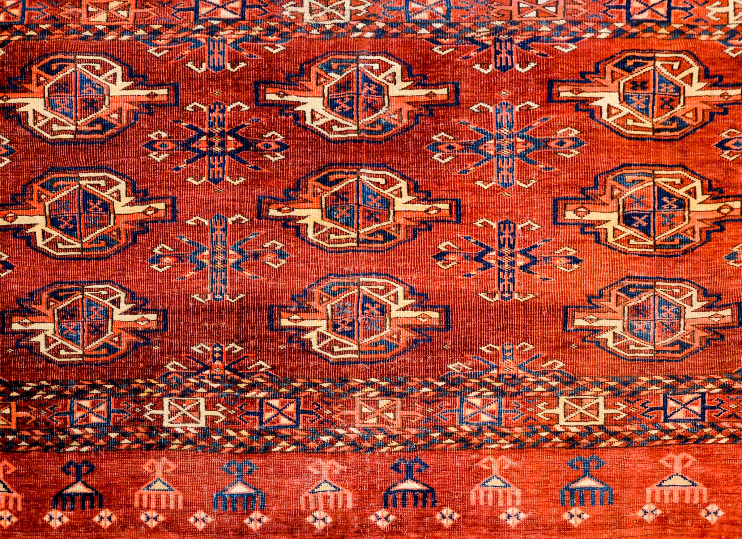 An early 20th century Persian Teke bag face rug with multiple geometric form shapes woven in indigo, crimson, and gold, on a bright crimson background surrounded by a complementary geometric patterned border.