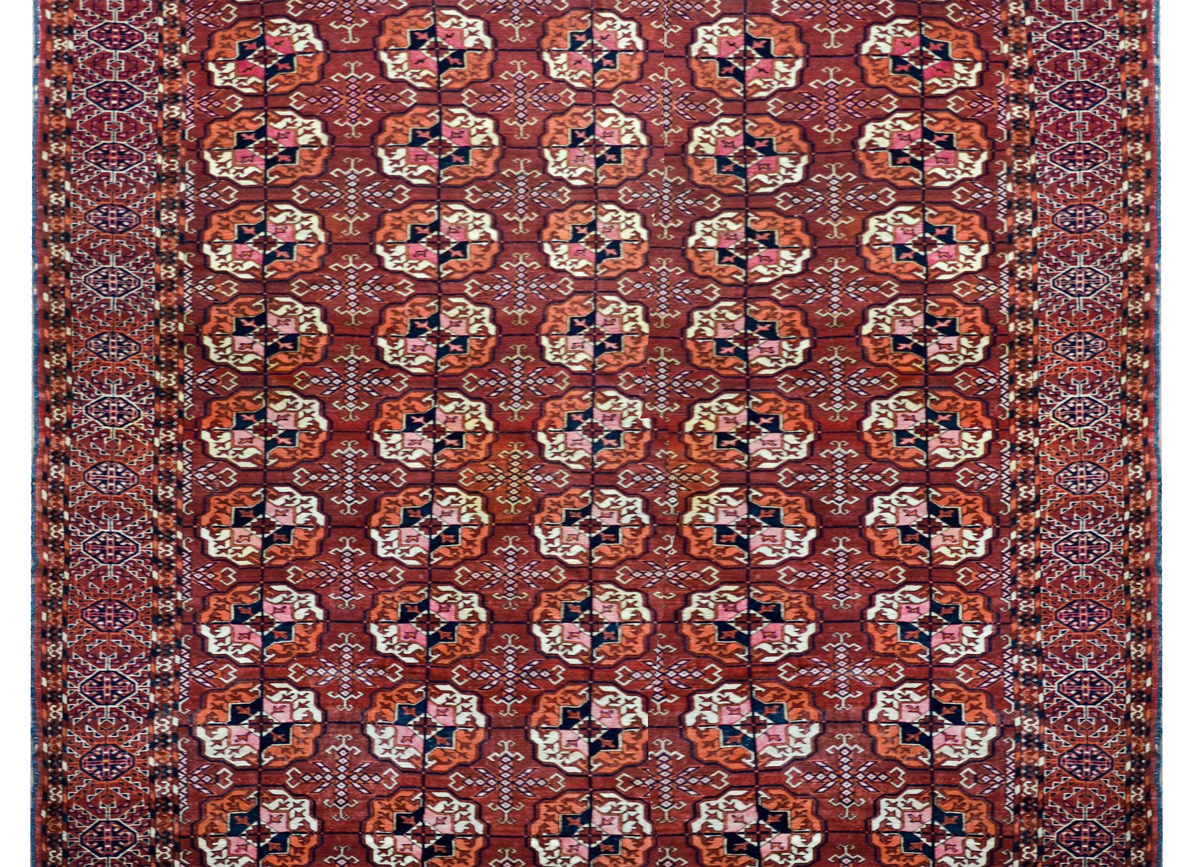A striking early 20th century Persian Teke rug with an all-over pattern with myriad geometric medallions woven in crimson, orange, white, and dark indigo, and surrounded by a wide geometric patterned border woven in similar colors as the field.