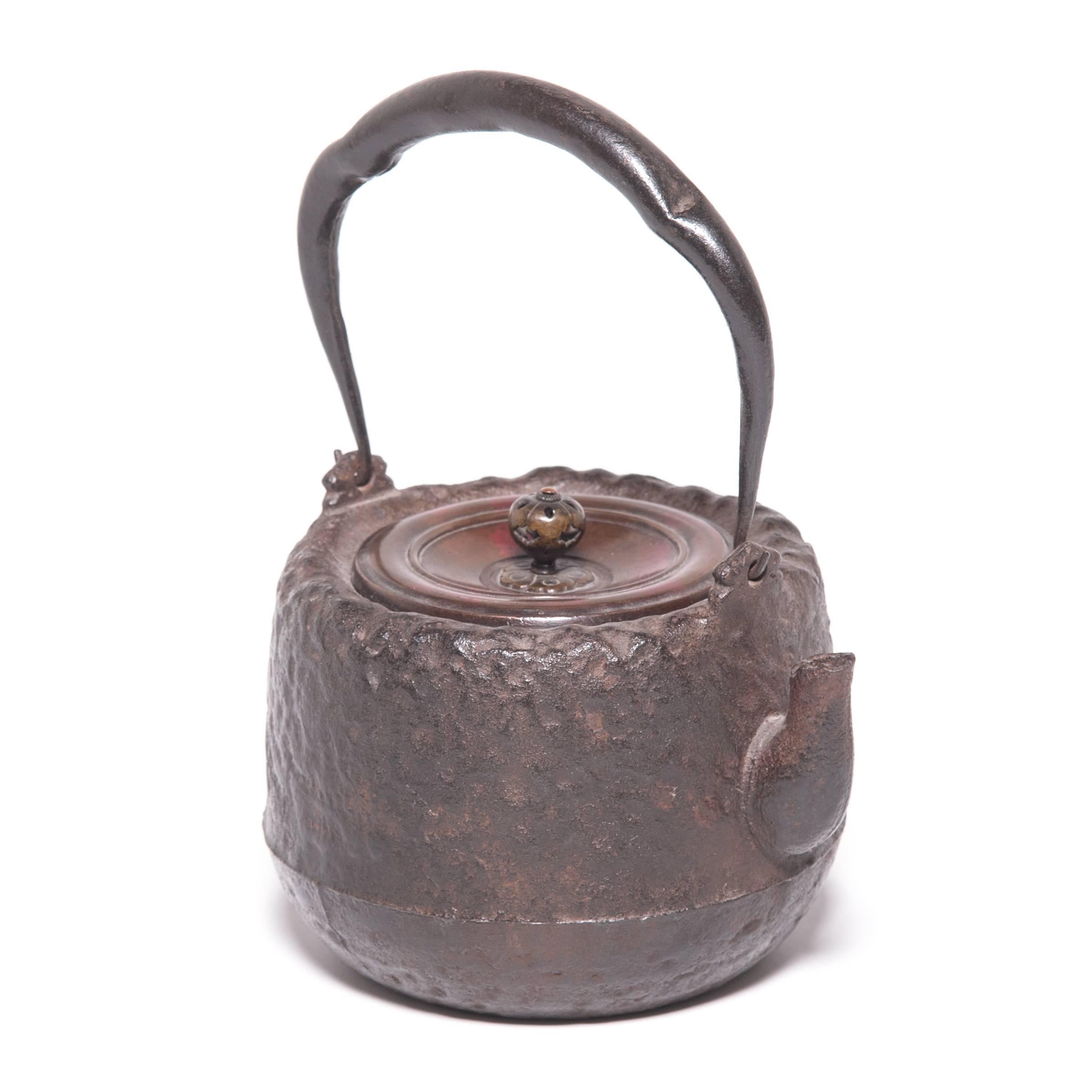 Decorated with an irregular, textured surface and an elegant, arched handle, this Japanese teapot was used to boil water for traditional tea ceremonies. Known as tetsubin, the kettle’s cast-iron construction is said to change the quality of the