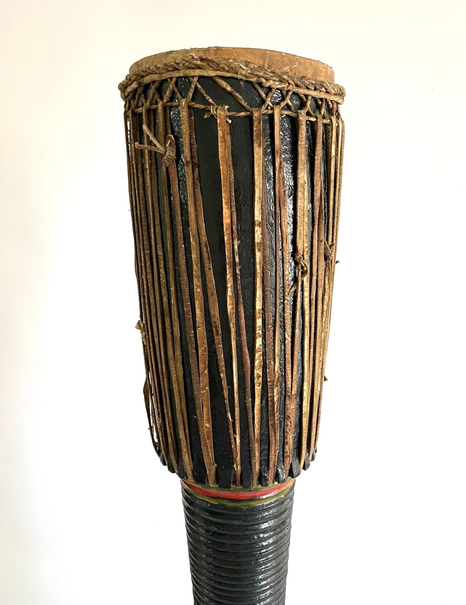 Ce tambour de temple élégamment sculpté était utilisé dans les temples bouddhistes. Il est sculpté dans du teck et laqué en noir avec des détails rayés rouges et verts. La partie supérieure et les sangles sont en cuir. Ces gigantesques tambours à