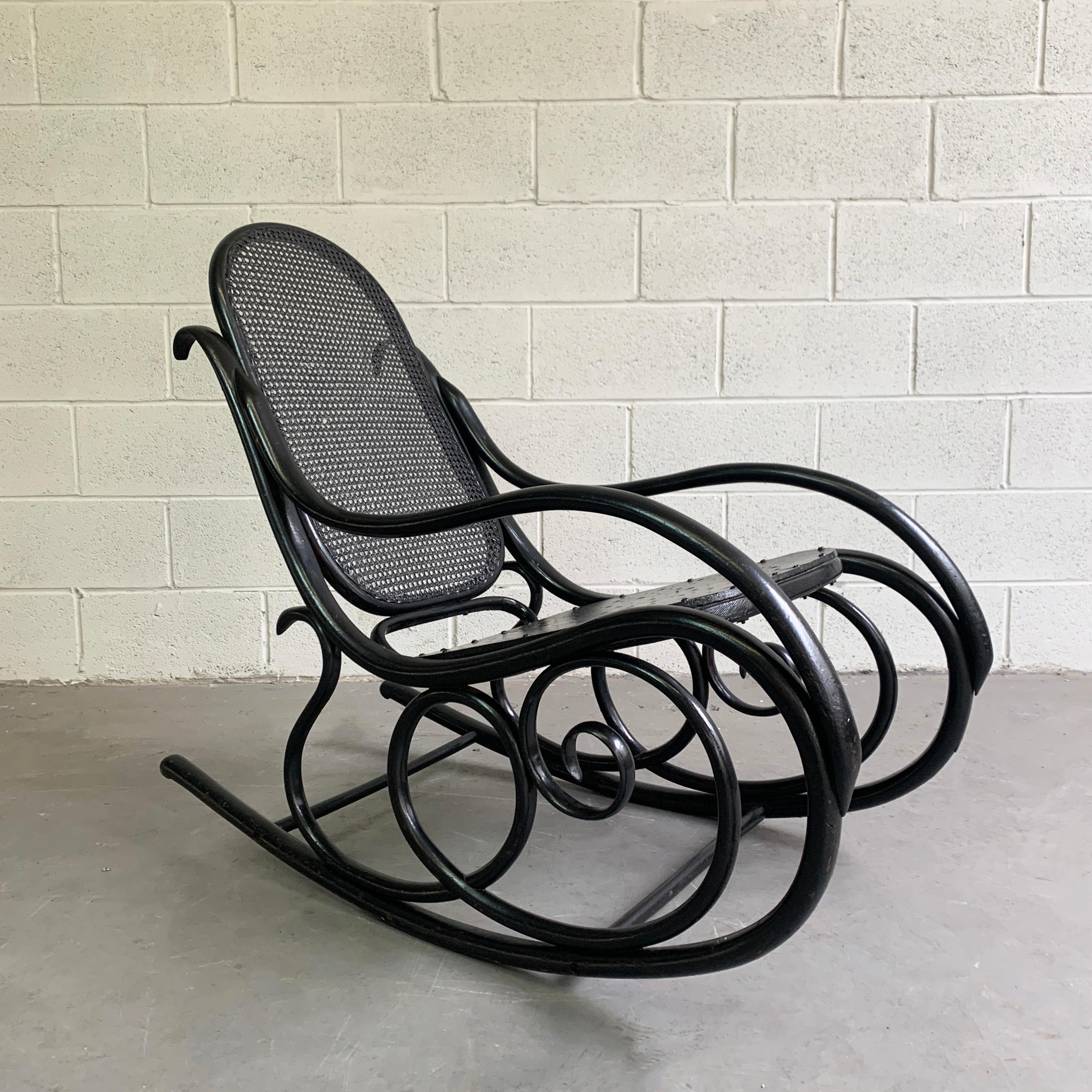 Early 20th century rocking chair by Thonet features a scrolled bentwood frame, caned back and perforated wood seat that slopes from 17.5 to 12 inches height.
