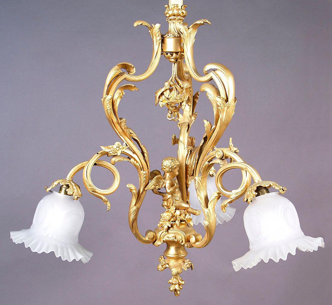 Early 20th century three-arm gilded bronze chandelier with cupid
A three-arm chandelier with cupid in the middle. The arms are shaped like plant stems, decorated with small flowers and finished with a lampshade holder in the form of chiseled