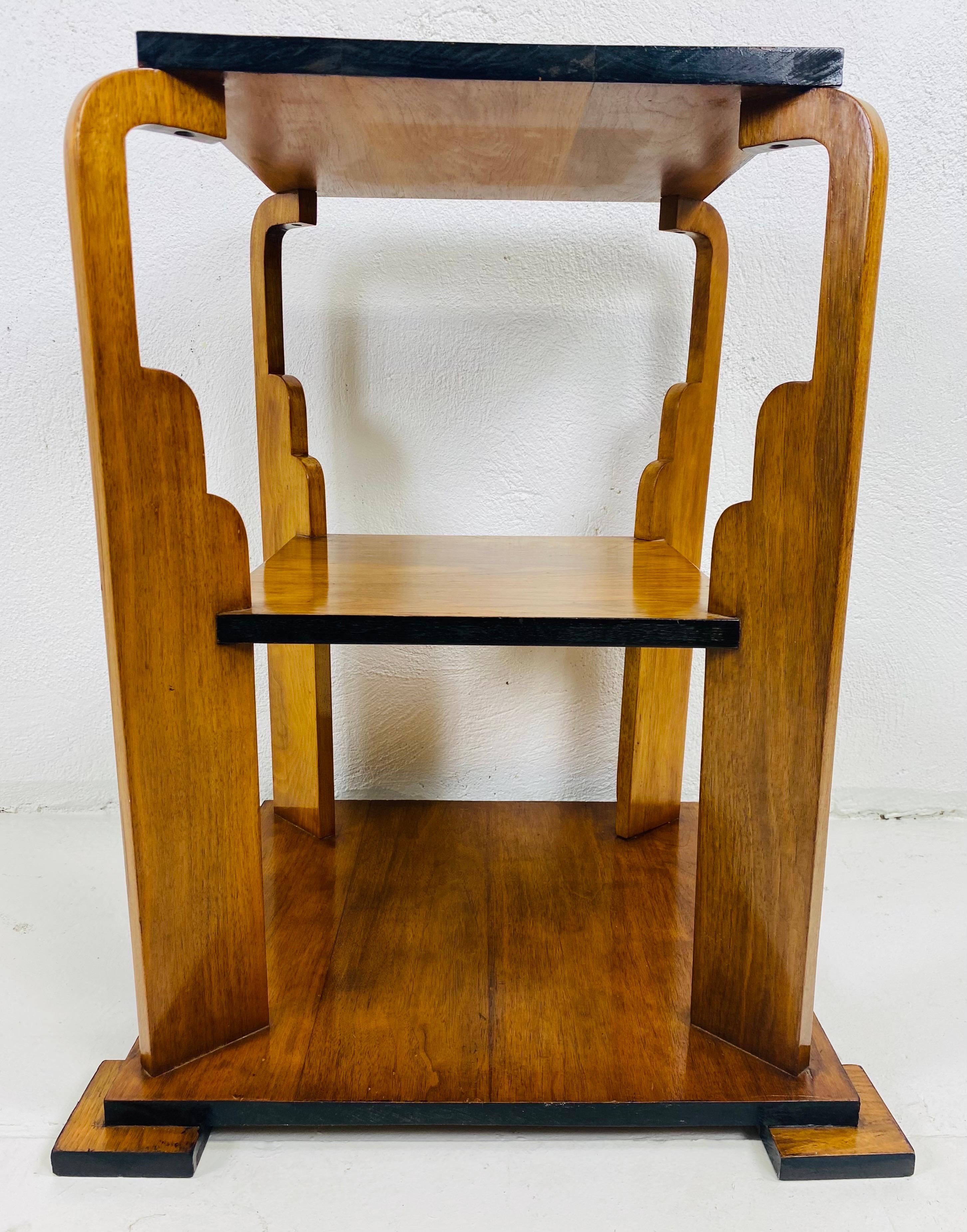 This is an early 20th century Art Deco three tiered side table. The side table has an architectural sensibility to its construction with four exaggerated columns that extend out from the corners. The table has a black laced edged border to each