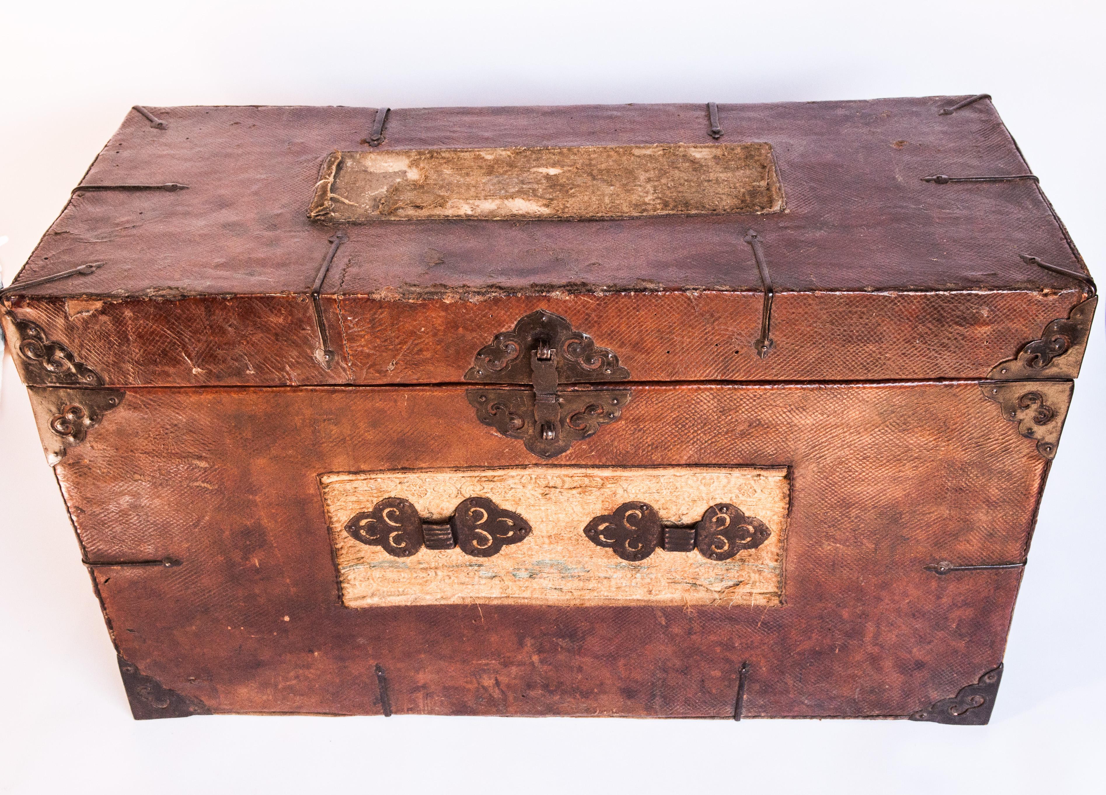 Early 20th century Tibetan leather chest with distressed silk tapestry panels.
This chest could have been used to store any manner of objects, from sacred to secular. It comprises original hand worked metal hardware, a rich patinated leather -