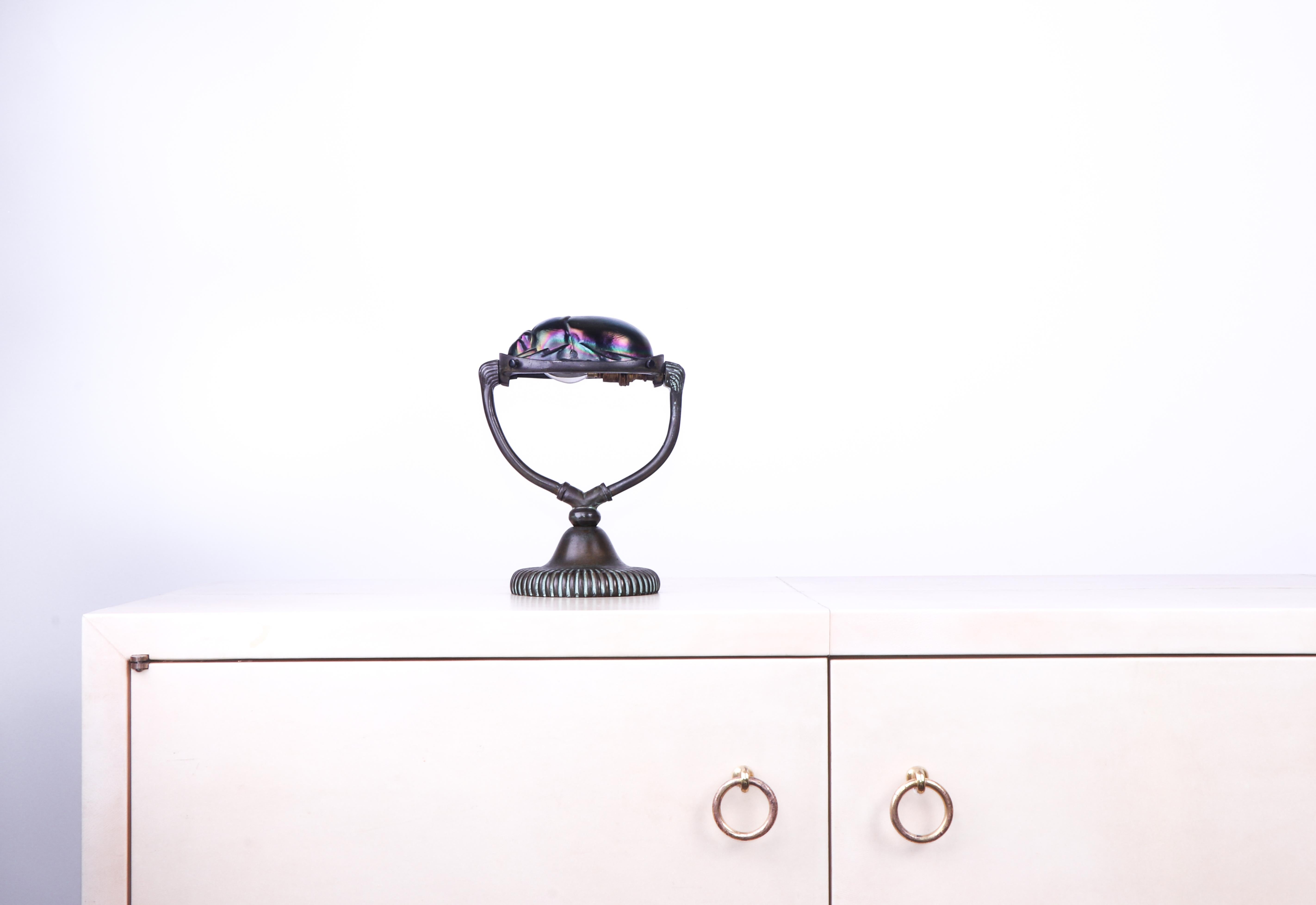 Rare and exquisite 'scarab' table lamp in the style of Tiffany Studios table lamps from the same period. 

This lamp is in excellent condition. It is composed of a bronze base and a glass scarab top; when the lamp is illuminated the latter gives off