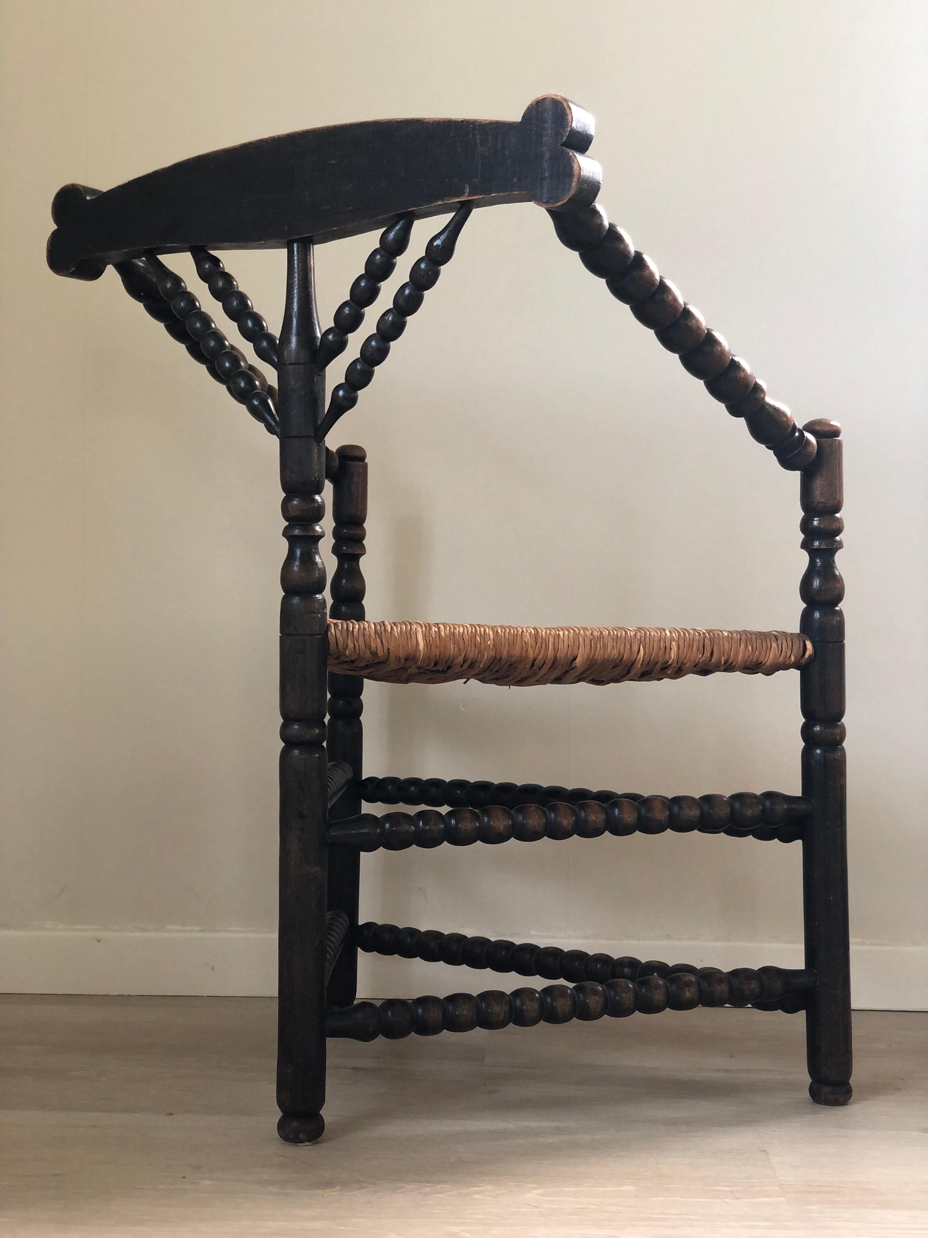 A beautifully crafted and sturdy three-legged corner chair from the United Kingdom, dating to the early 20th century. Made of walnut, this bobbin chair features finely carved details on the legs and armrests. The seat is handwoven rush, adding to