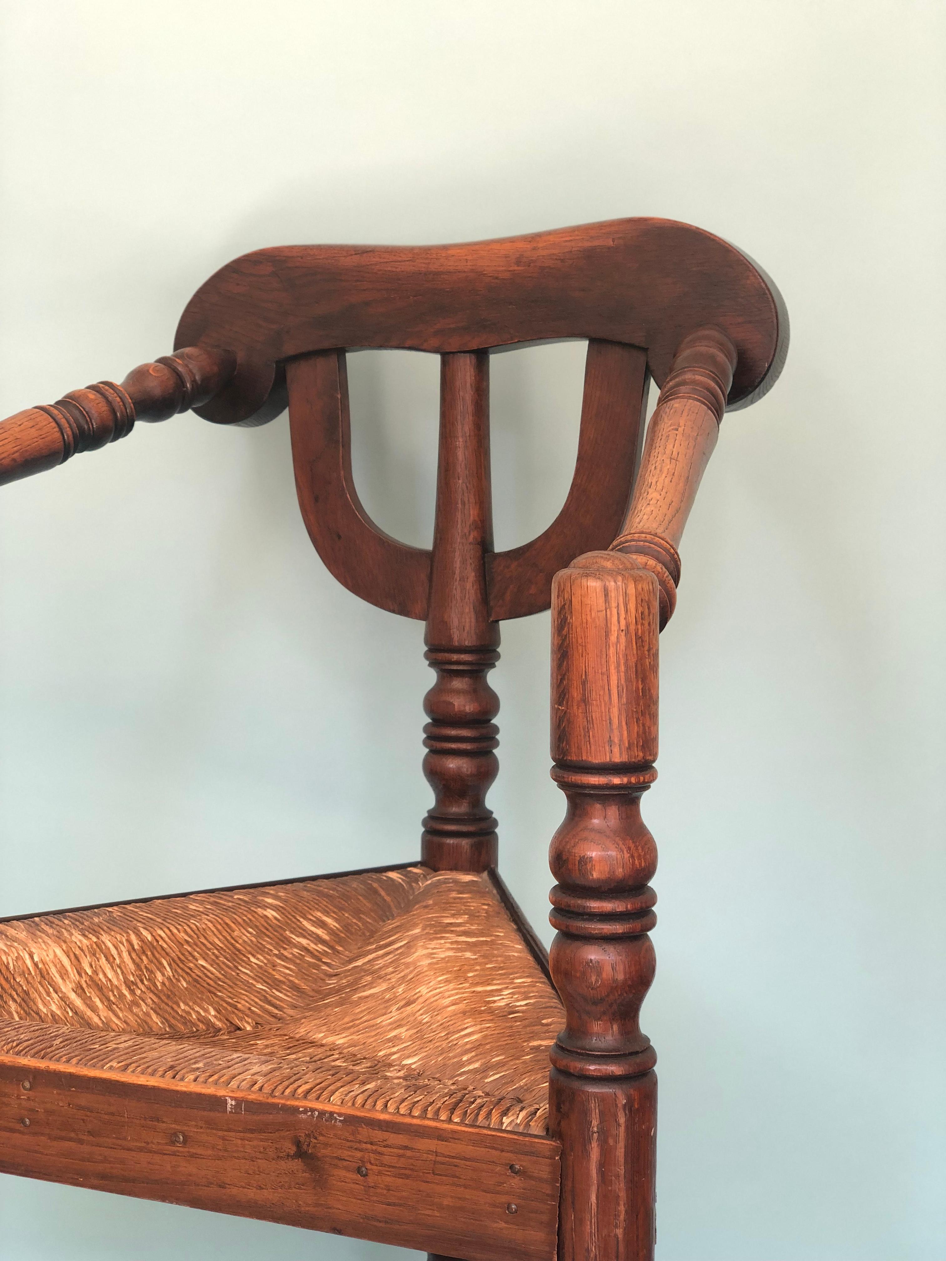 A beautiful and sturdy corner chair from the United Kingdom, early 20th century. The Walnut chair has carved details in the legs and armrests and has a rush seat. In good condition.

Object: Chair
Design: Unknown
Style: Antique,
Period: