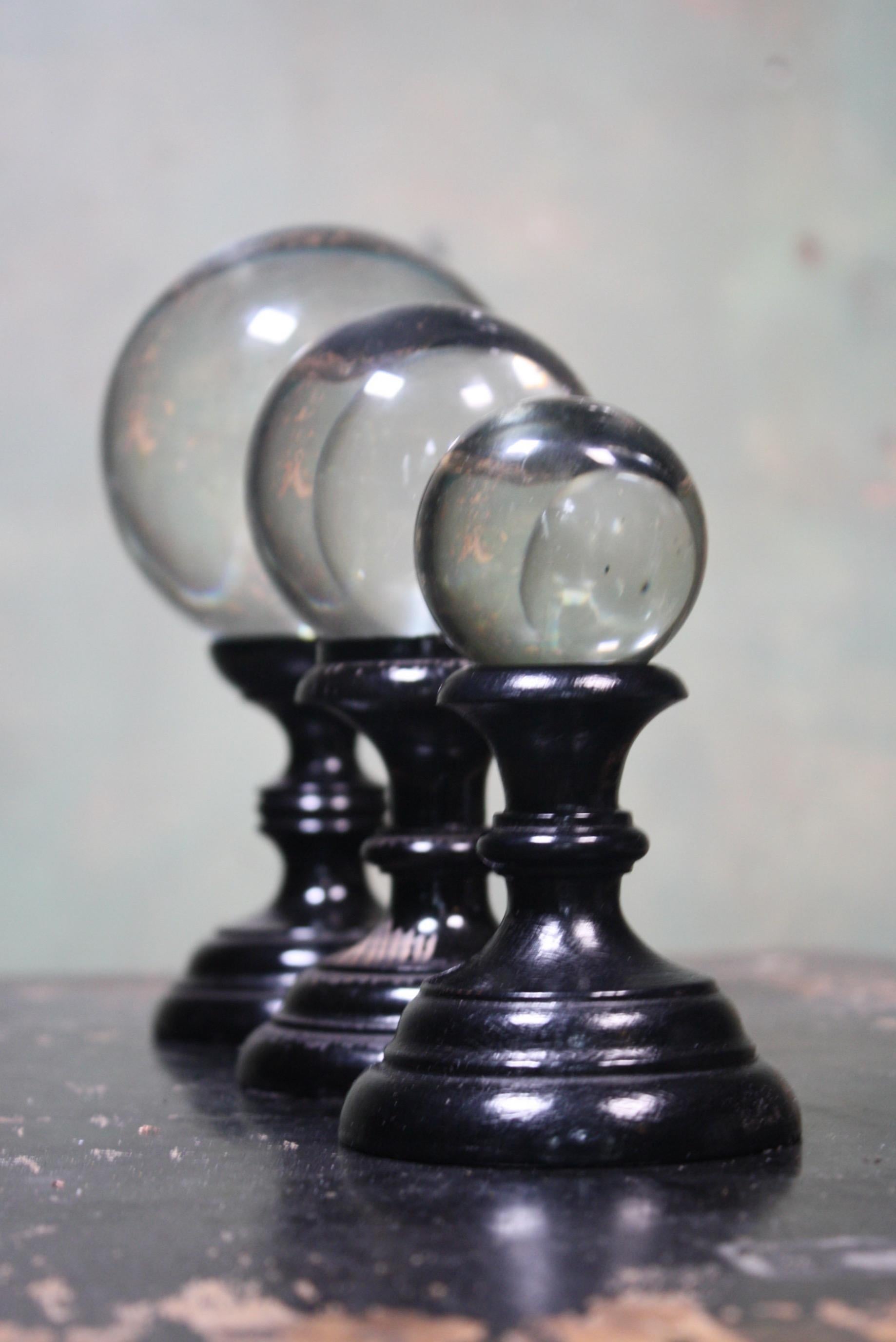 A trio of early 20th century glass optical spheres, on ebonized stands.

The smallest of the three stands is a later replacement, all the glass globes are in great order no chips or bruising, very minimal surface wear if any. The two original