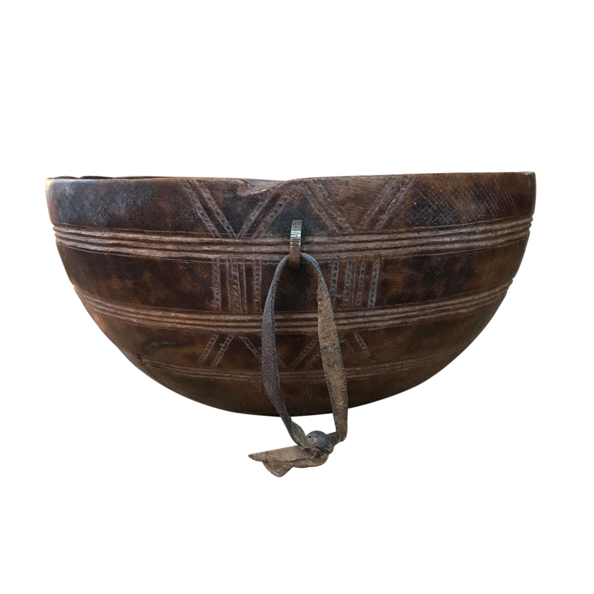 An early 20th century Tuareg bowl carved on a single piece of wood incised with a geometric pattern, and with a small brass ring with a leather strap. The Tuareg are nomadic pastoralists who inhabit the Saharan region of Northern Africa. Because so