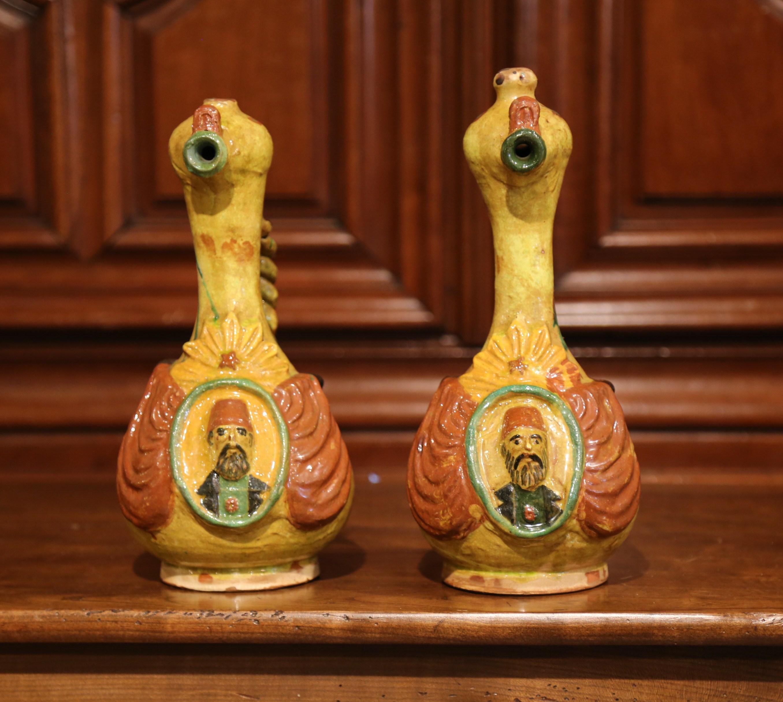 Bring colors to your kitchen with these antique glazed oil pitchers; created in Turkey, circa 1920, each colorful pitcher features a weave shape handle, and a carved Turkish figure medallion on the front. Both pieces are in very good condition with