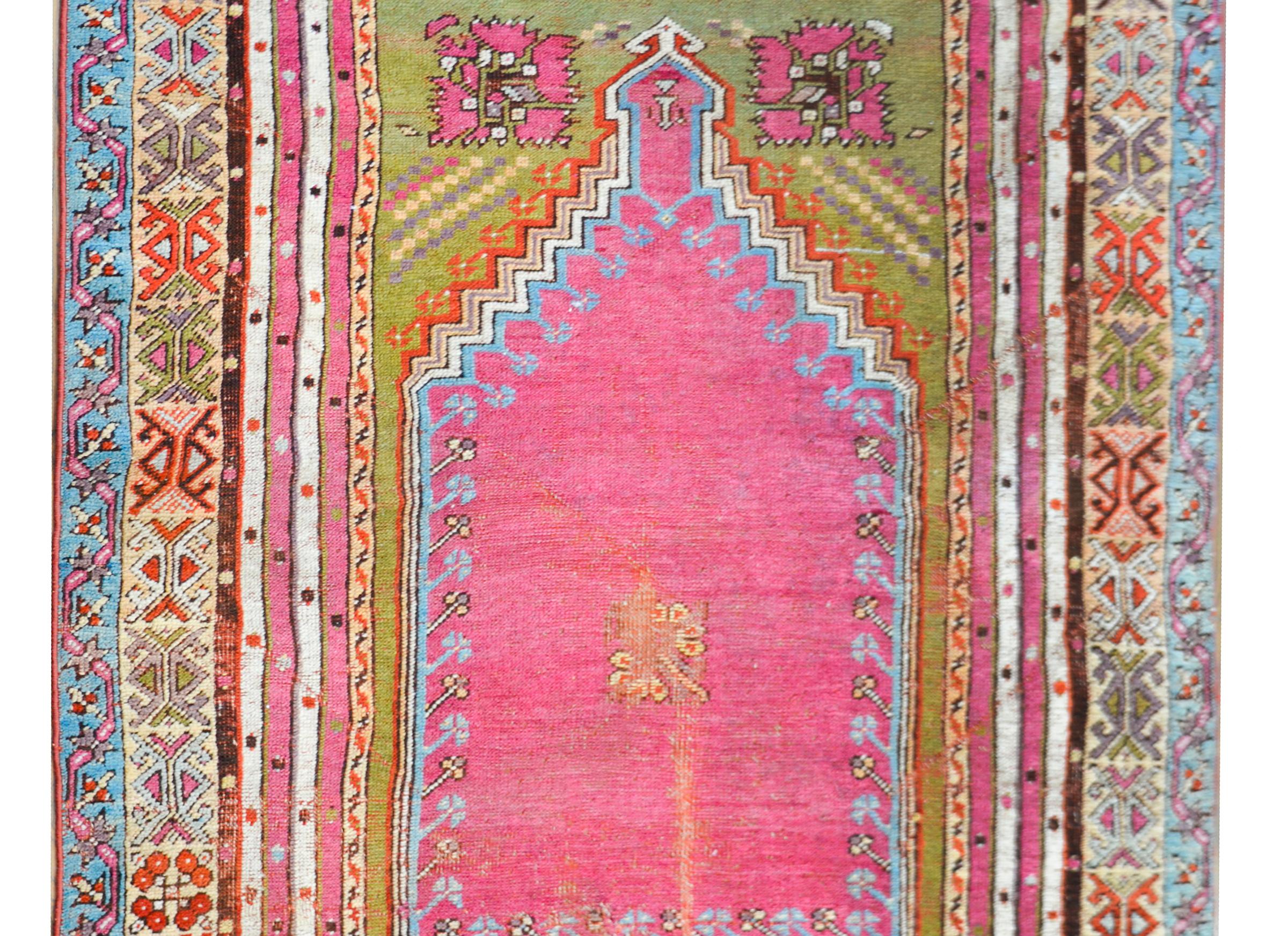 A beautiful early 20th century Turkish Konya Prayer rug with a wonderful color palette including a bright pink center surrounded by multiple thin stylized floral patterned stripes woven in teal, coral, yellow, chartreuse green, and white.