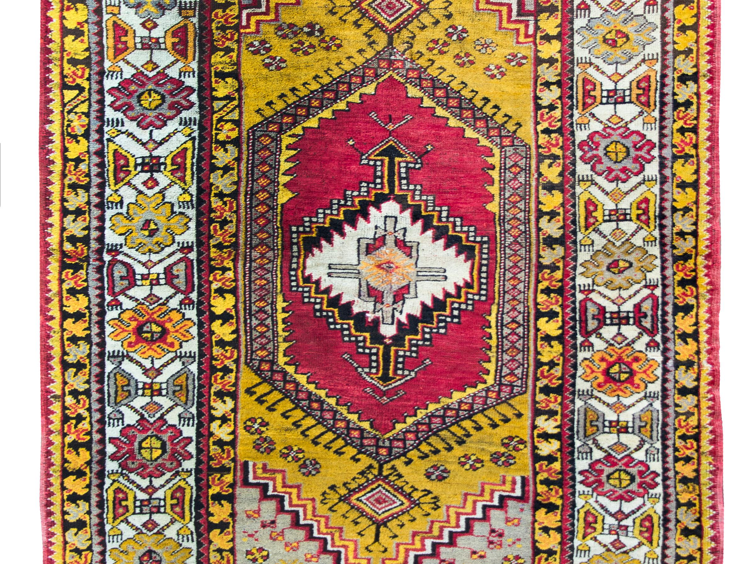 A bold and brilliant early 20th century Turkish Konya rug with a tribal pattern containing a central geometric medallion living amidst a field of more geometric stylized floral patterns, and all surrounded by a wonderful border with repeated