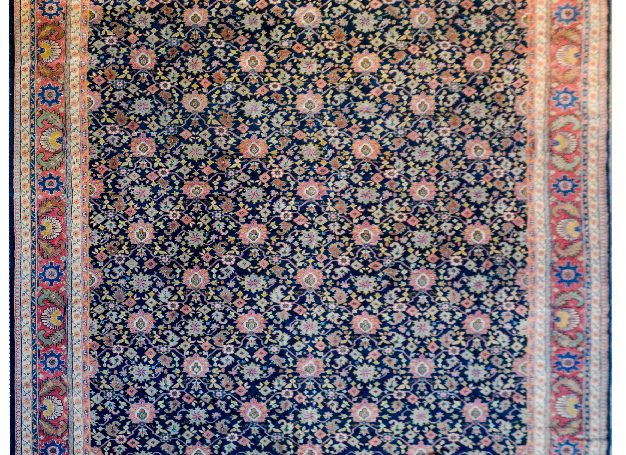 An exquisite early 20th century Turkish Mahal style rug with an all-over lattice pattern with large and small flowers woven in pink, gold, salmon, and green, all on a dark indigo background. The border is wide with large central stripe with a bold