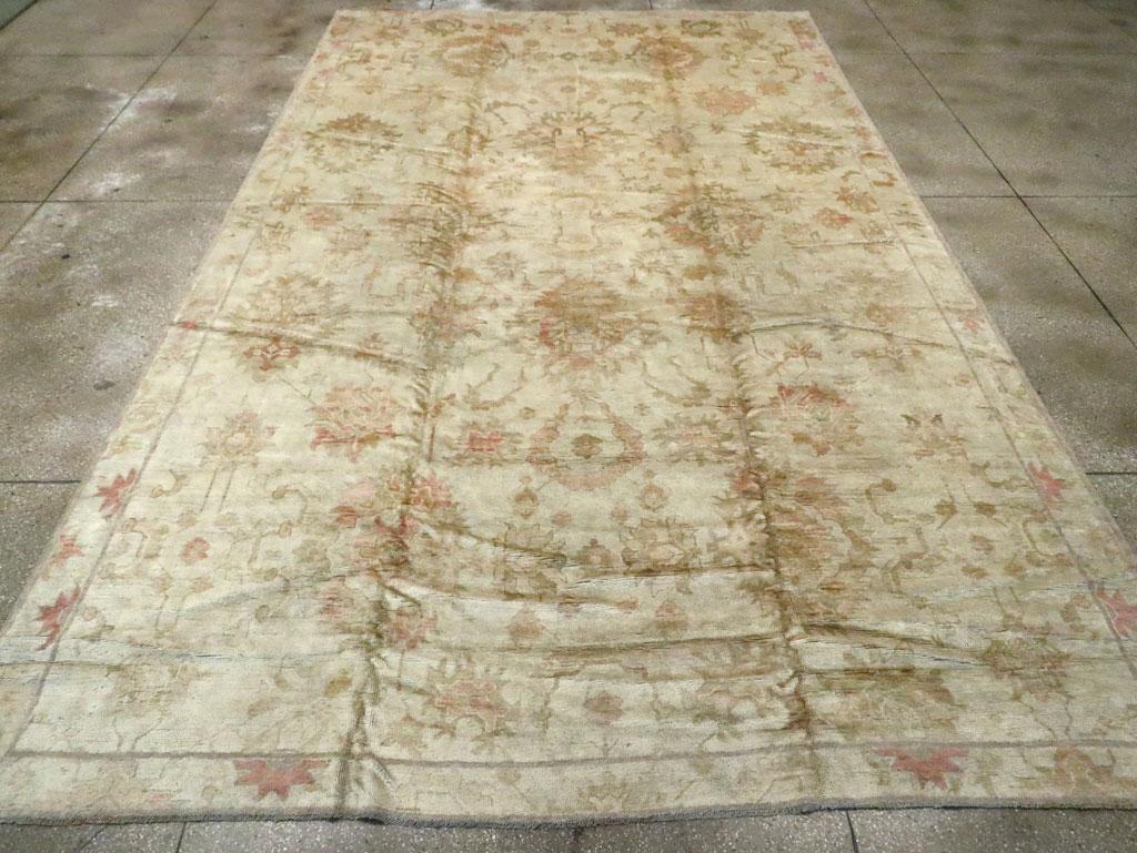 An antique Turkish Oushak large carpet. This carpet is almost all field, no border. The pearl ground extends across the entire carpet and the field displays a loose, open rendition of the Harshang design of large rust palmettes with the addition of