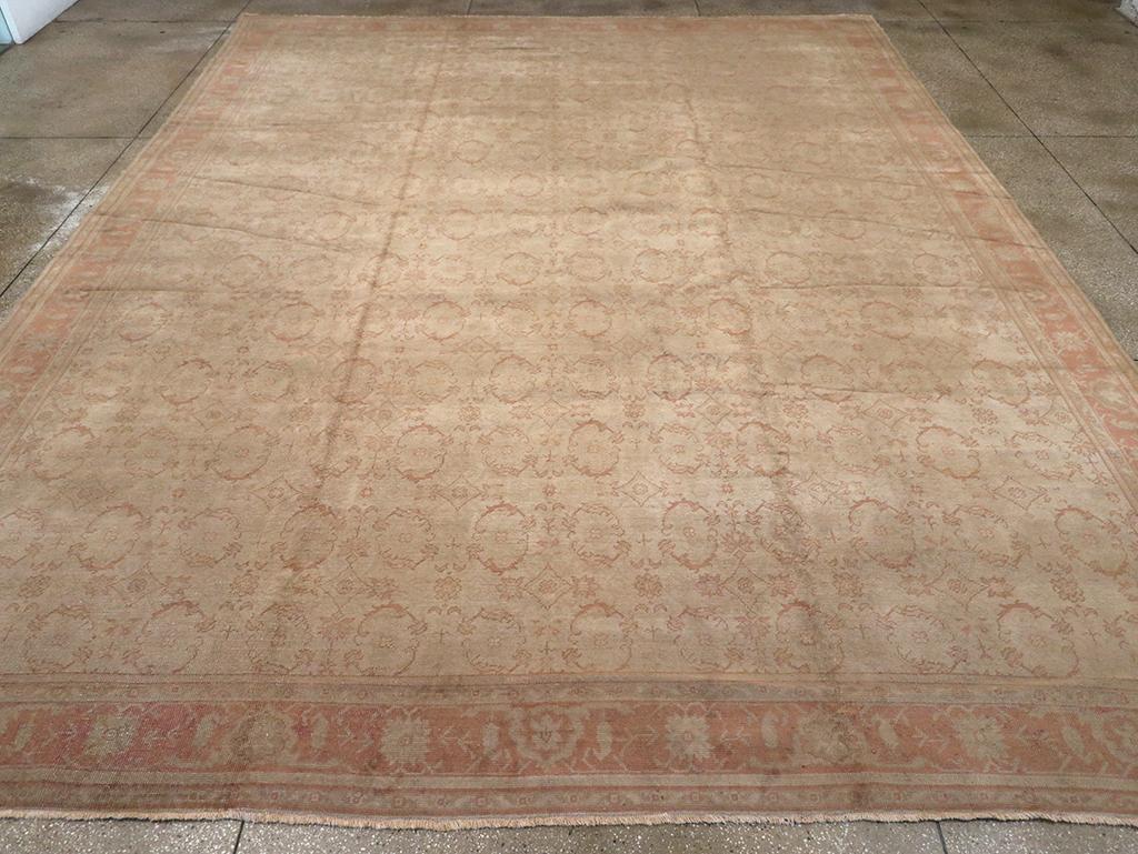Un grand tapis antique turc Oushak. De petits ovales ouverts aux contours bruns sont soigneusement espacés sur le champ beige de ce tapis turc occidental à poils hauts. Le système de bordures étroites permet de créer un cadre de retraite.

Noué à la