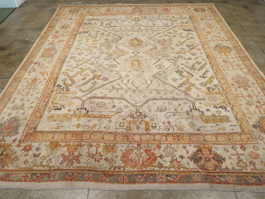 An antique Turkish Oushak large carpet. The golden ivory field of this west Turkish workshop carpet displays two ragged palmettes centering a fragmented branch, stem and leaf pattern set diagonally and horizontally. The drawing is angular and bold.