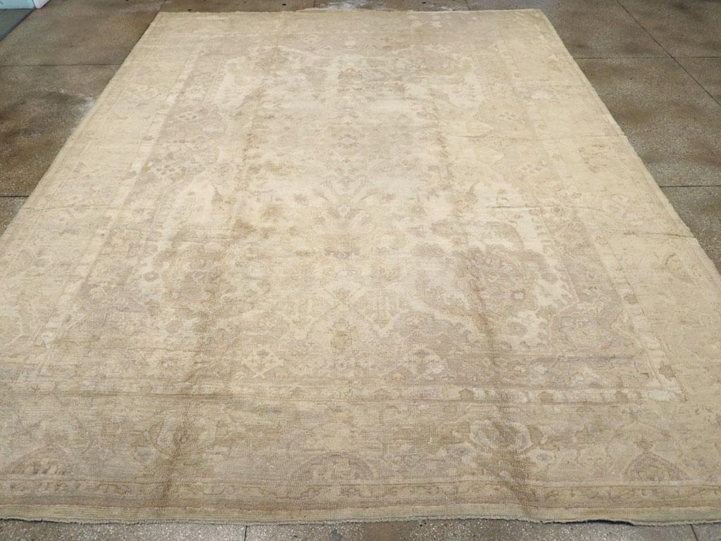 An antique Turkish Oushak large room size carpet. This west Anatolian workshop carpet is a study in ivory and beige tones. An unusual feature is an inner field surround with its rounded side intrusions, almost like a picture frame. A fountain-like